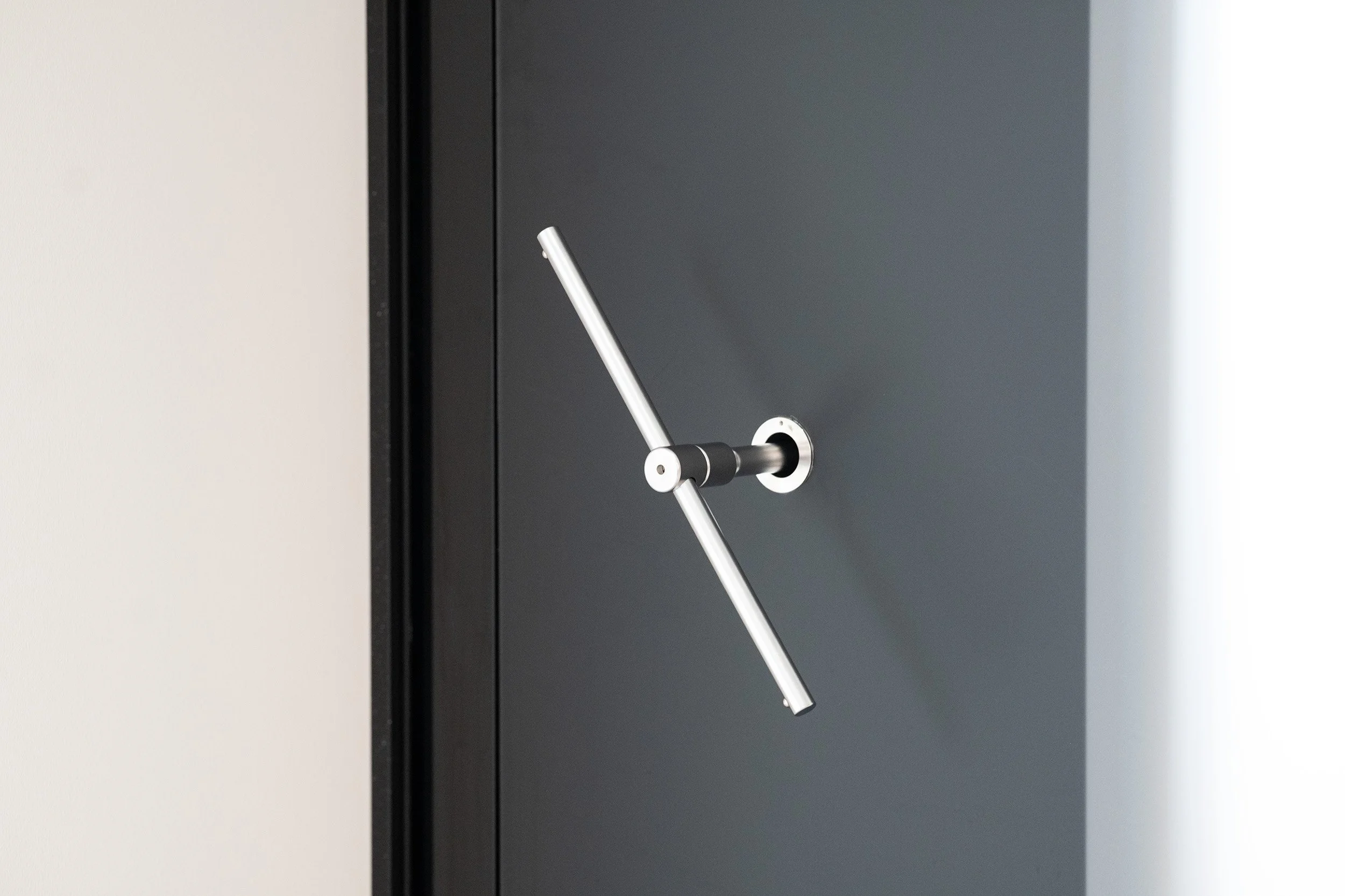 Modern door handle with a diagonal metal bar attached to a dark gray door.