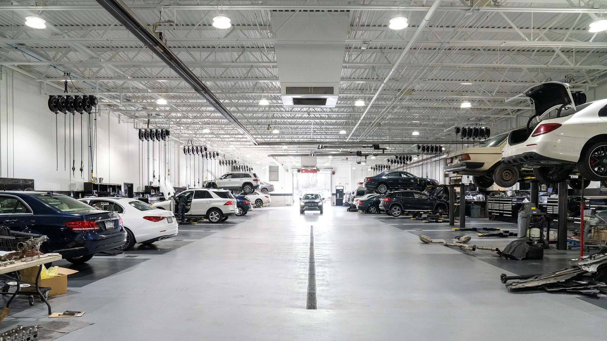 Car repair shop with multiple cars on lifts, service bays, and tools, in a spacious, well-lit industrial setting.