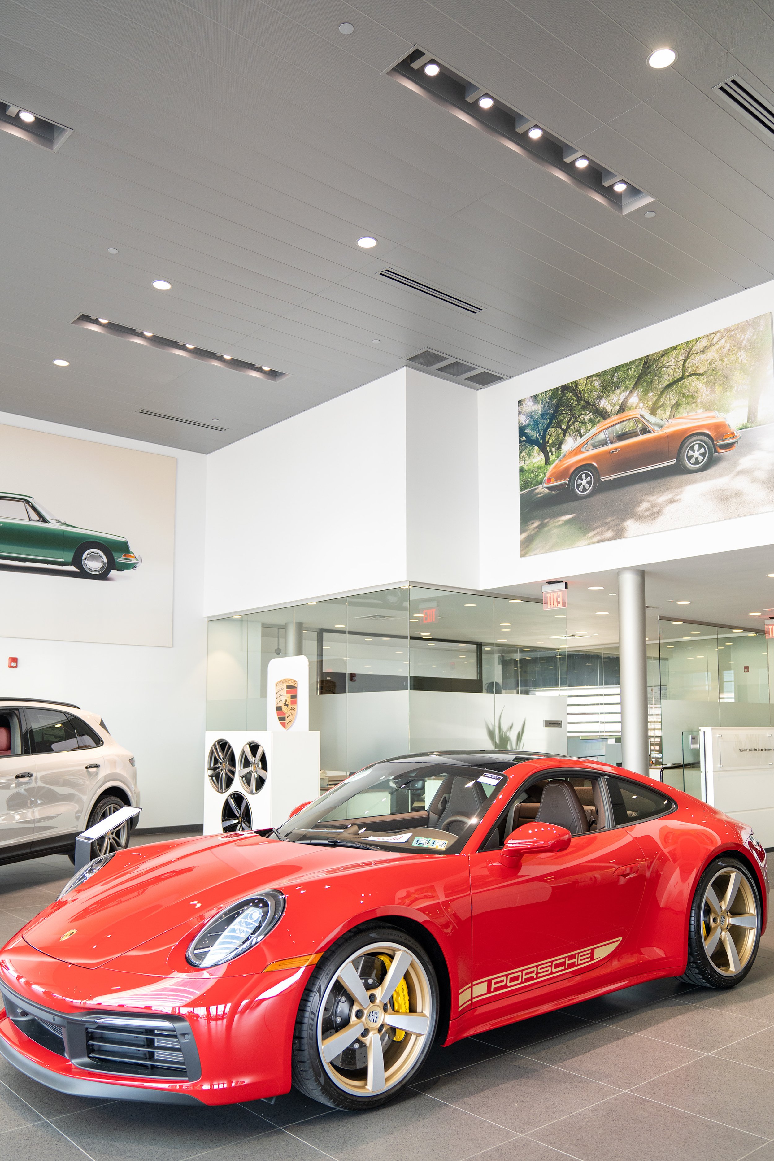 A red Porsche sports car displayed inside a car showroom with photos of classic cars on the wall behind it.