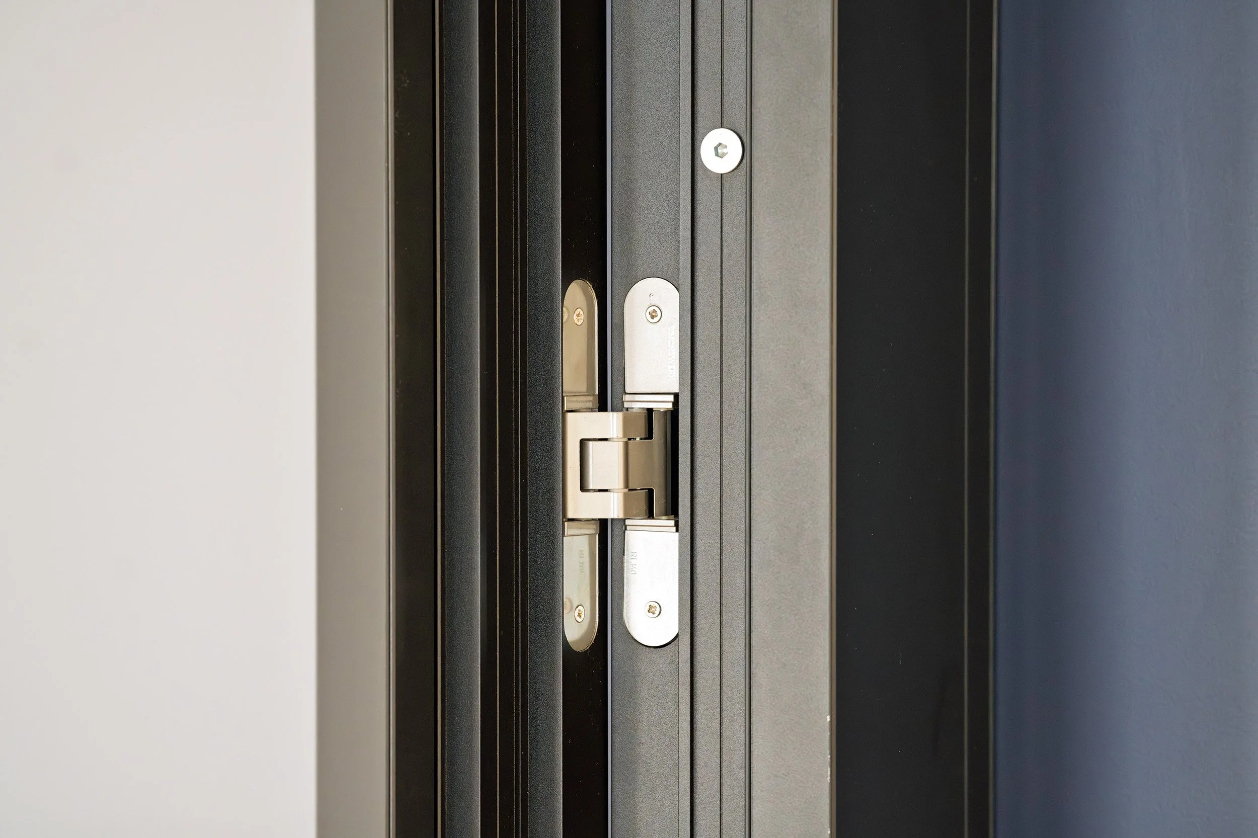 Close-up of a metal door latch and lock mechanism on a black door, with white, gray, and blue walls around it.