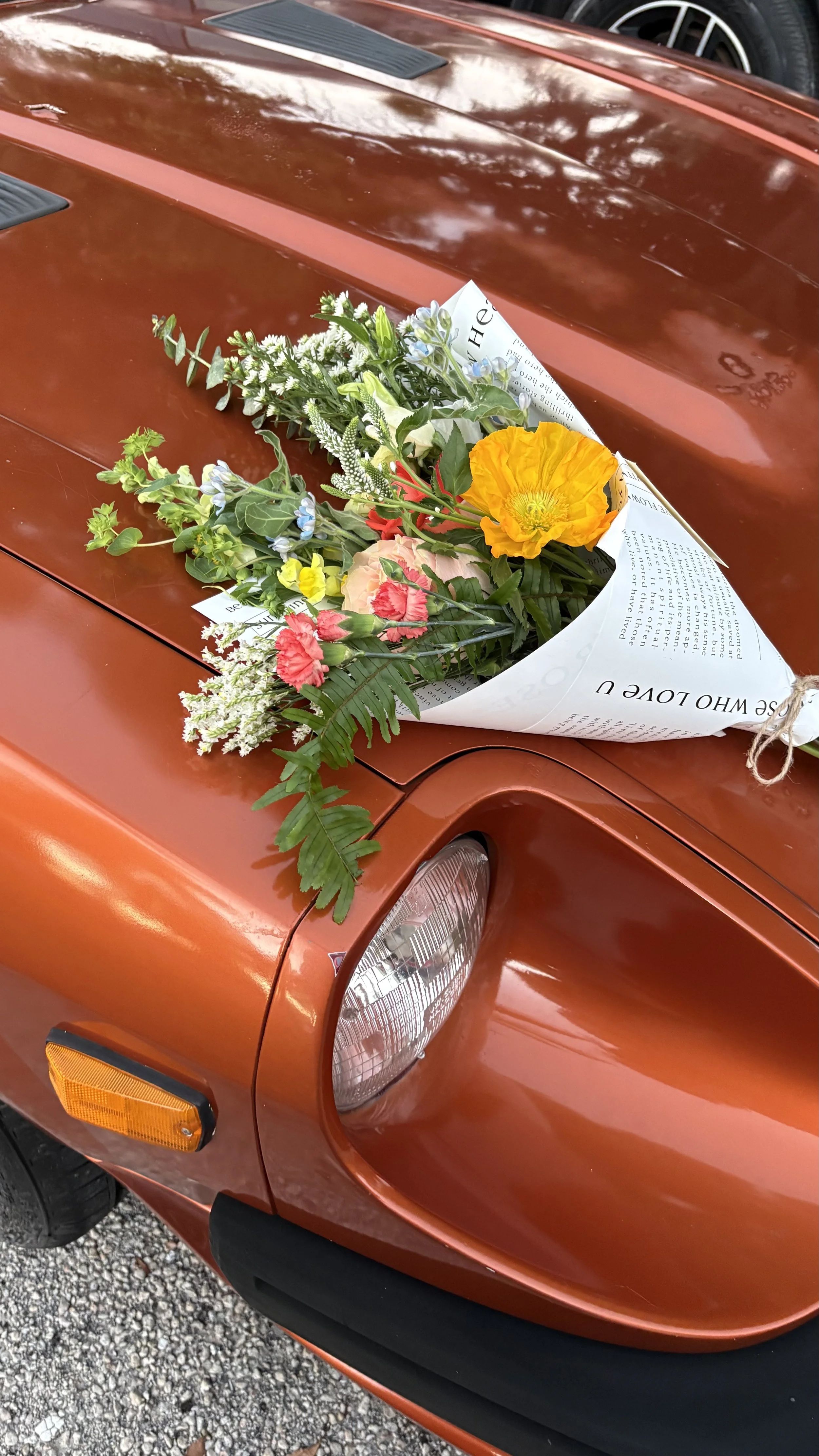 A bouquet of colorful flowers placed on the hood of an orange vintage car.