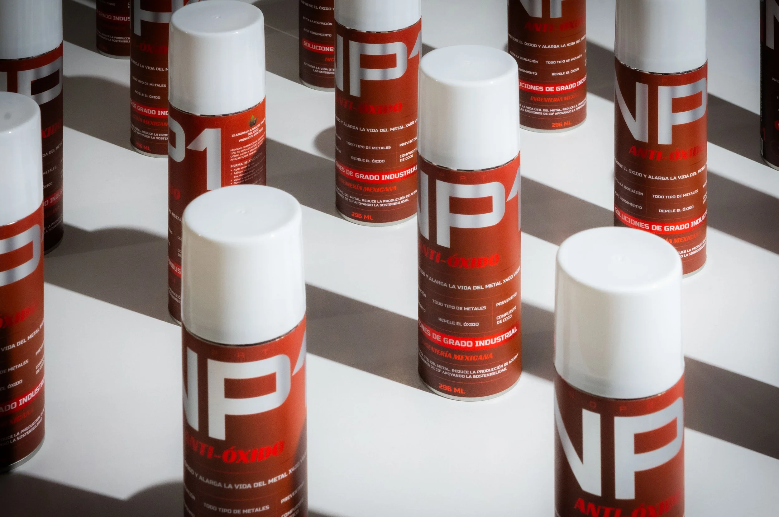 Several cans of anti-oxidant spray with red and white labels arranged on a white surface, casting shadows.