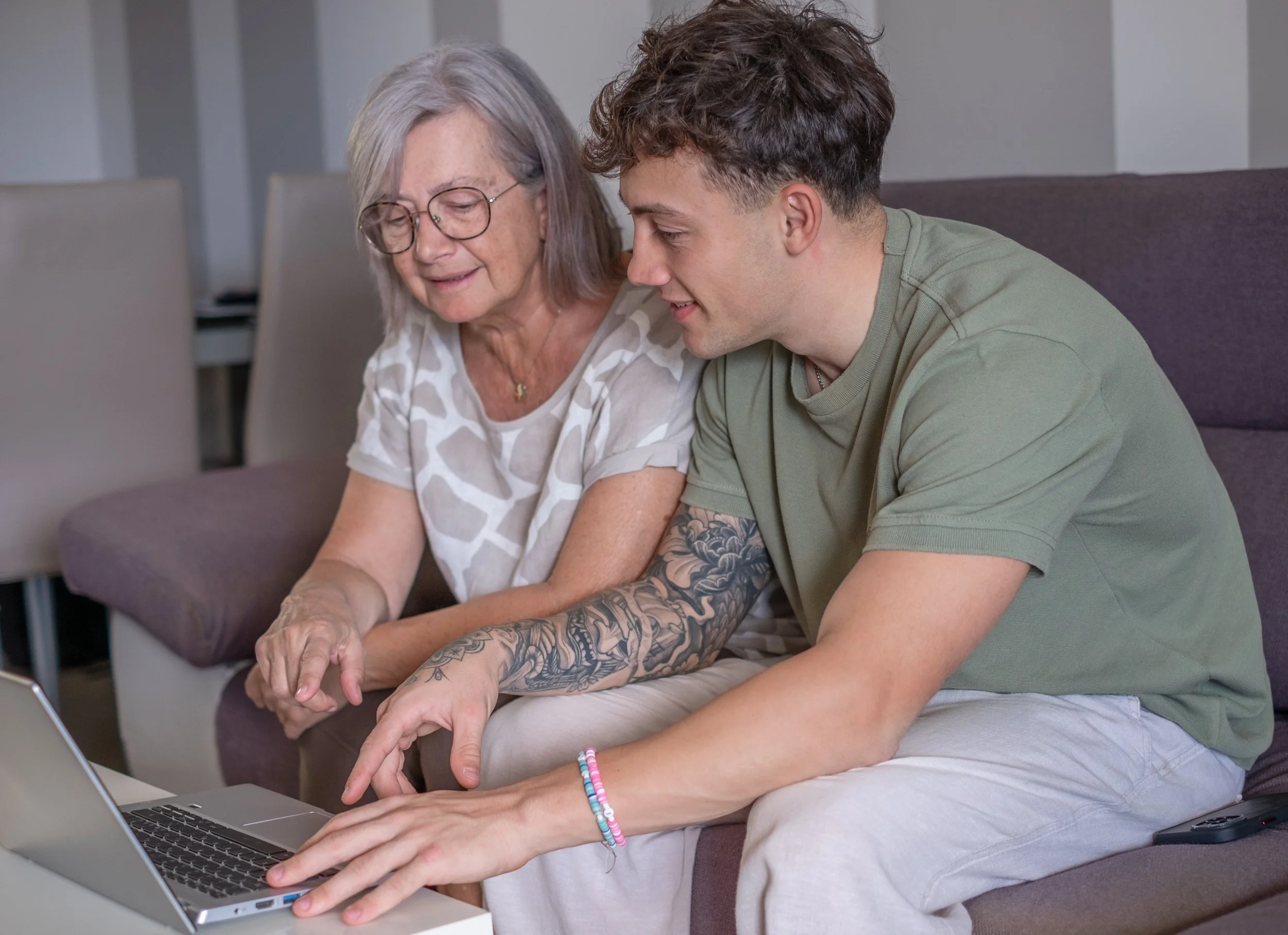 Jüngere Person hilft älterer Person bei Arbeit auf dem Computer