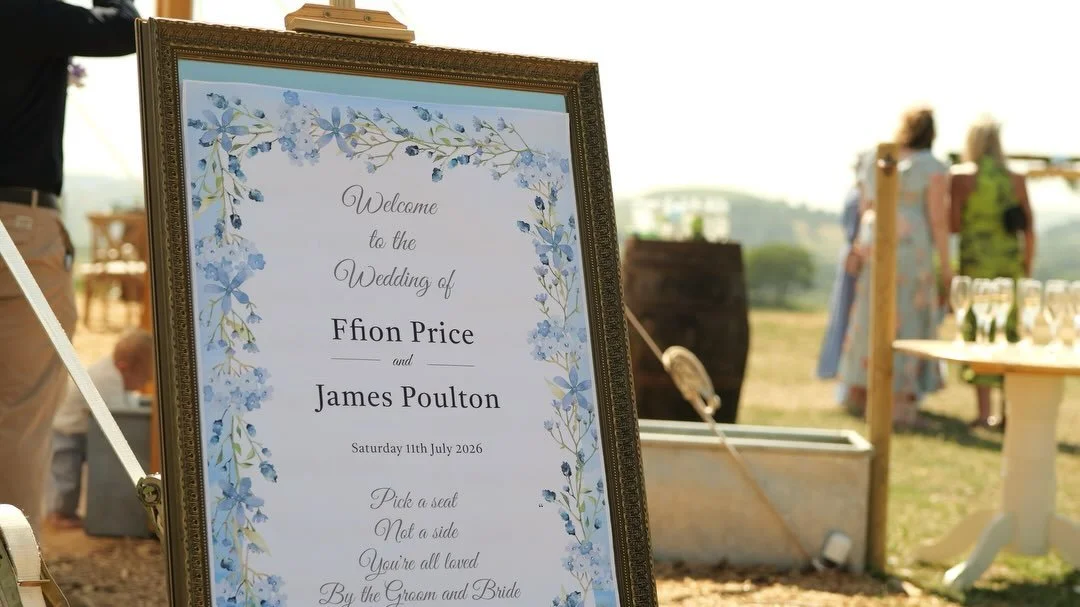 Wedding sign with floral border welcoming guests to the wedding of Ffion Price and James Poulton on July 11, 2026, in an outdoor setting.