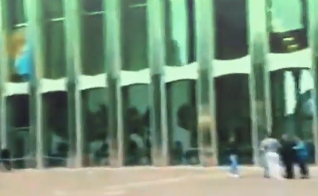 Blurred image of a glass building with reflections, and a group of people walking outside.