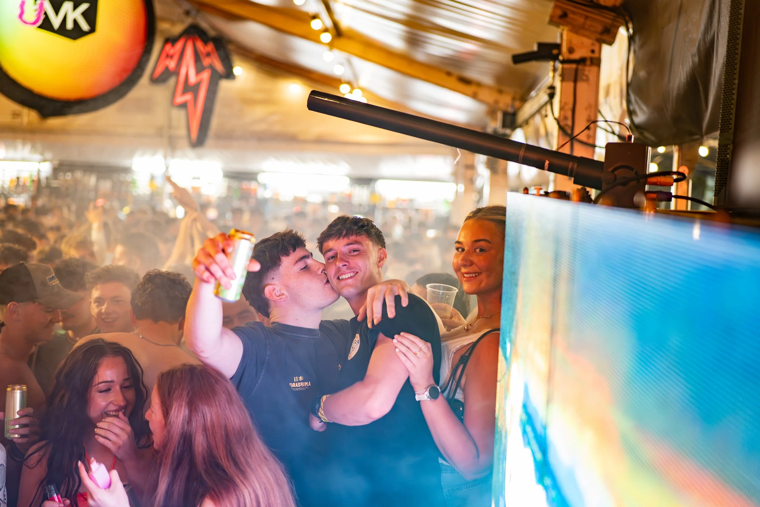 Group of friends celebrating at a party or club with colorful lights, smiling, hugging, and holding drinks.