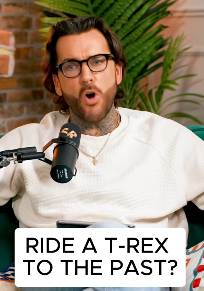 A man with dark hair, glasses, and tattoos on his neck, speaking into a microphone with a 'SP' logo, sitting on a green sofa, with a brick wall and large green plant in the background, captioned 'Ride a T-Rex to the Past?'