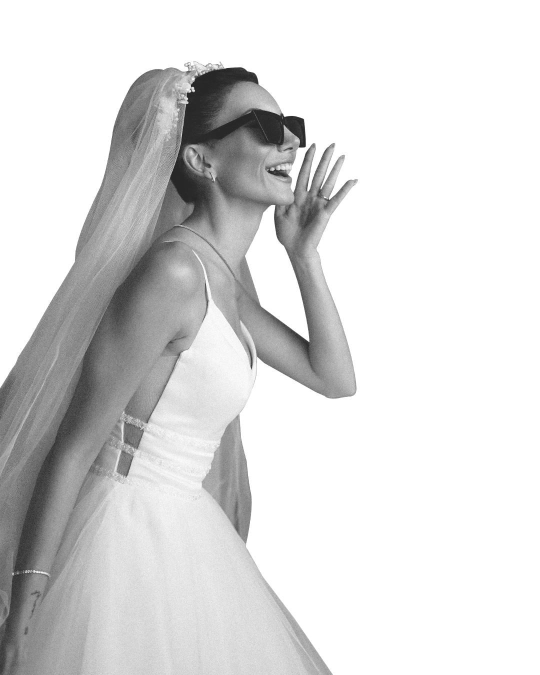 A smiling woman in a wedding dress and veil, wearing sunglasses, laughing with her hand near her face.