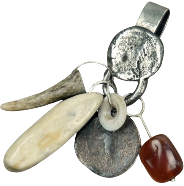 A collection of various charms and objects, including a small animal tooth, a shell, metal discs, and a red stone, attached to a keyring.