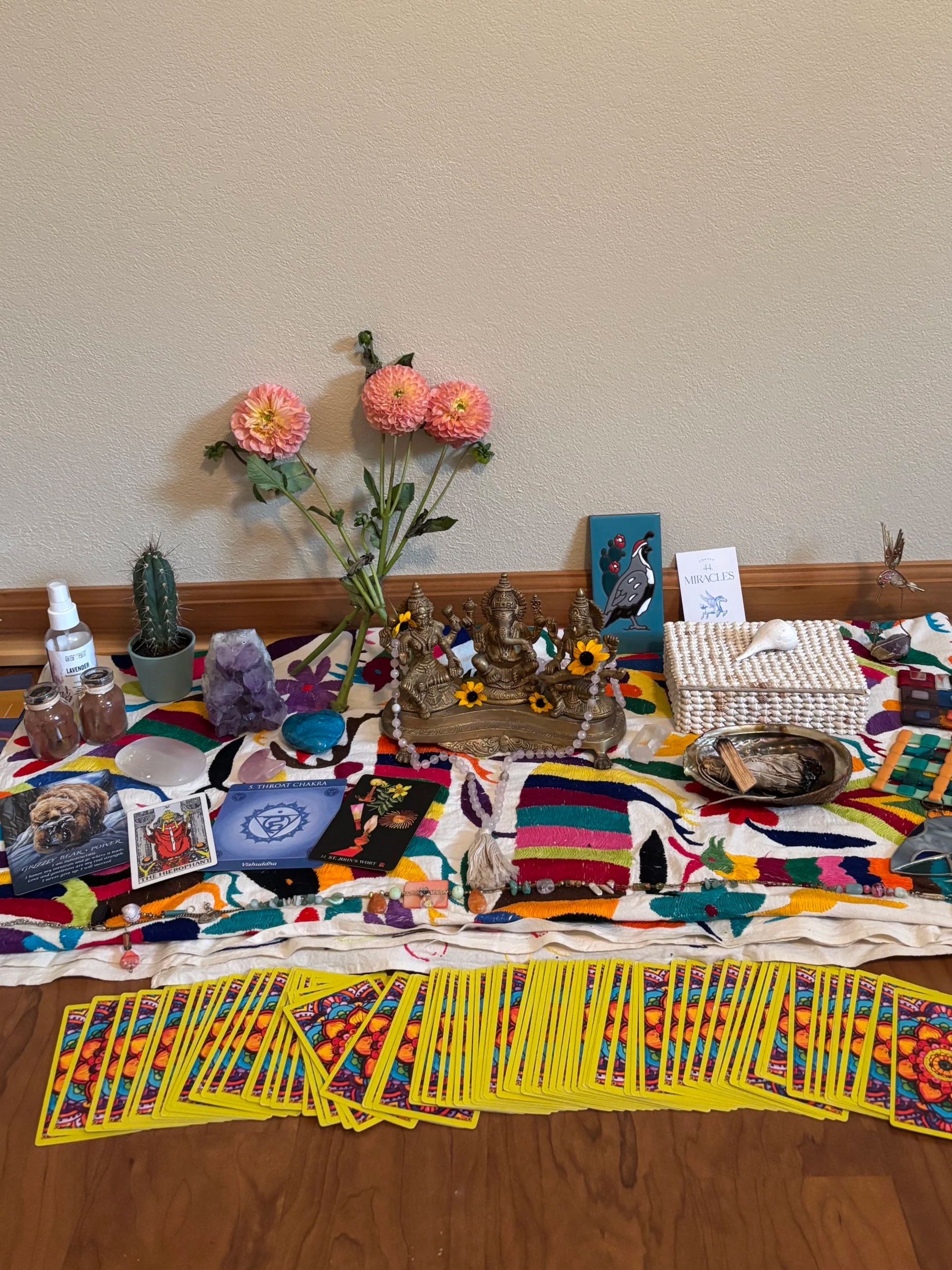 An altar with colorful fabric, tarot cards, crystals, candles, flowers, and spiritual objects for meditation or ritual.