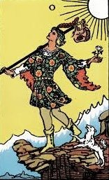A woman in a floral dress dances on rocks near the ocean with a dog on a leash and a cat on the ground, under a sunny sky.