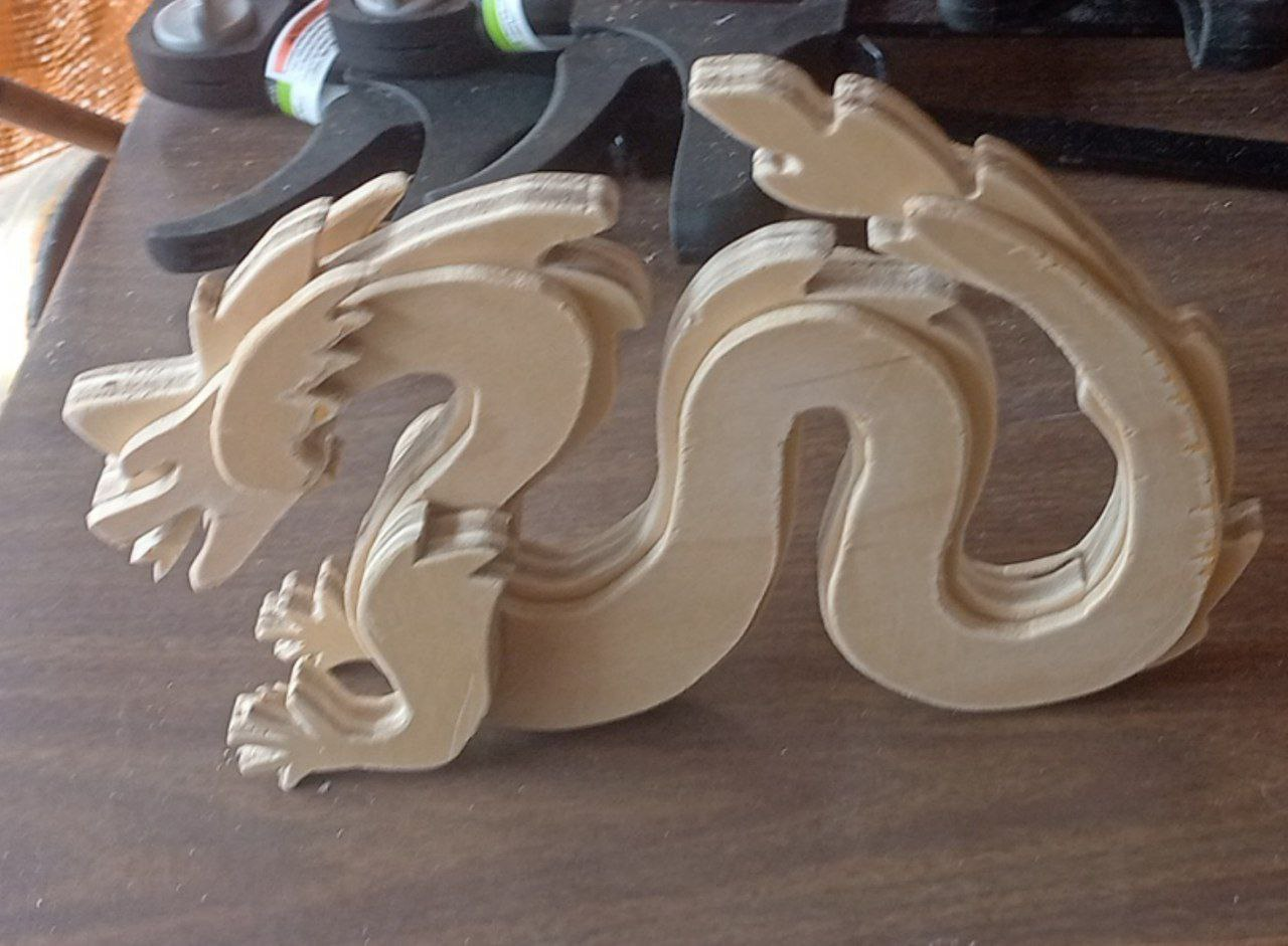 Wooden carved dragon figure on a wooden surface with paint bottles in the background.