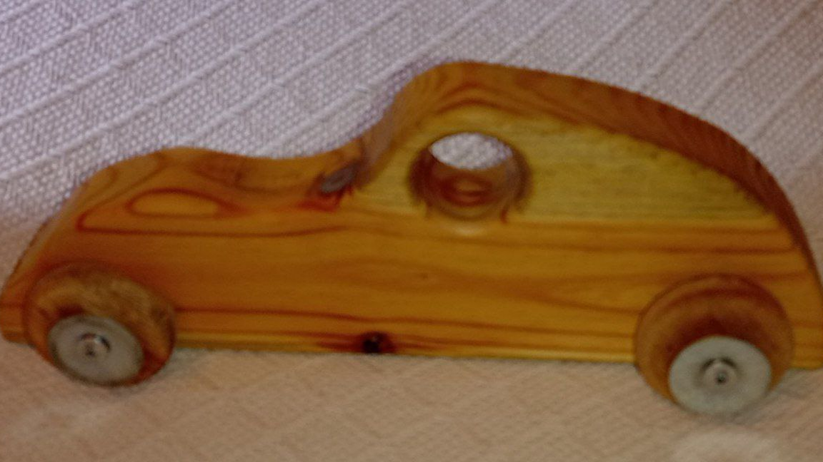 Wooden toy car with four small wheels on a light fabric surface.
