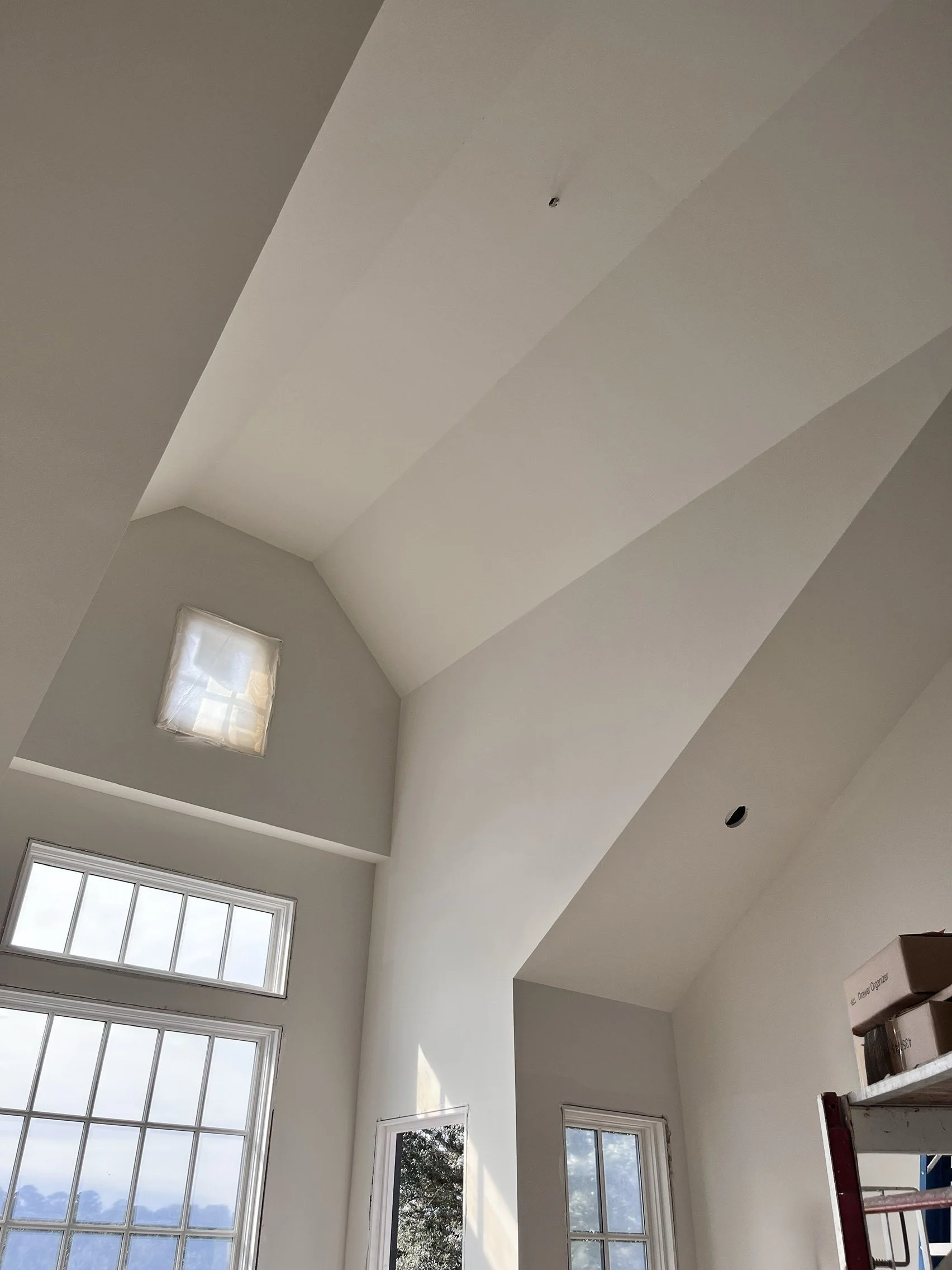 Interior shot of a room with high, sloped ceiling and large windows, with some boxes on a red shelf visible in the bottom right corner.
