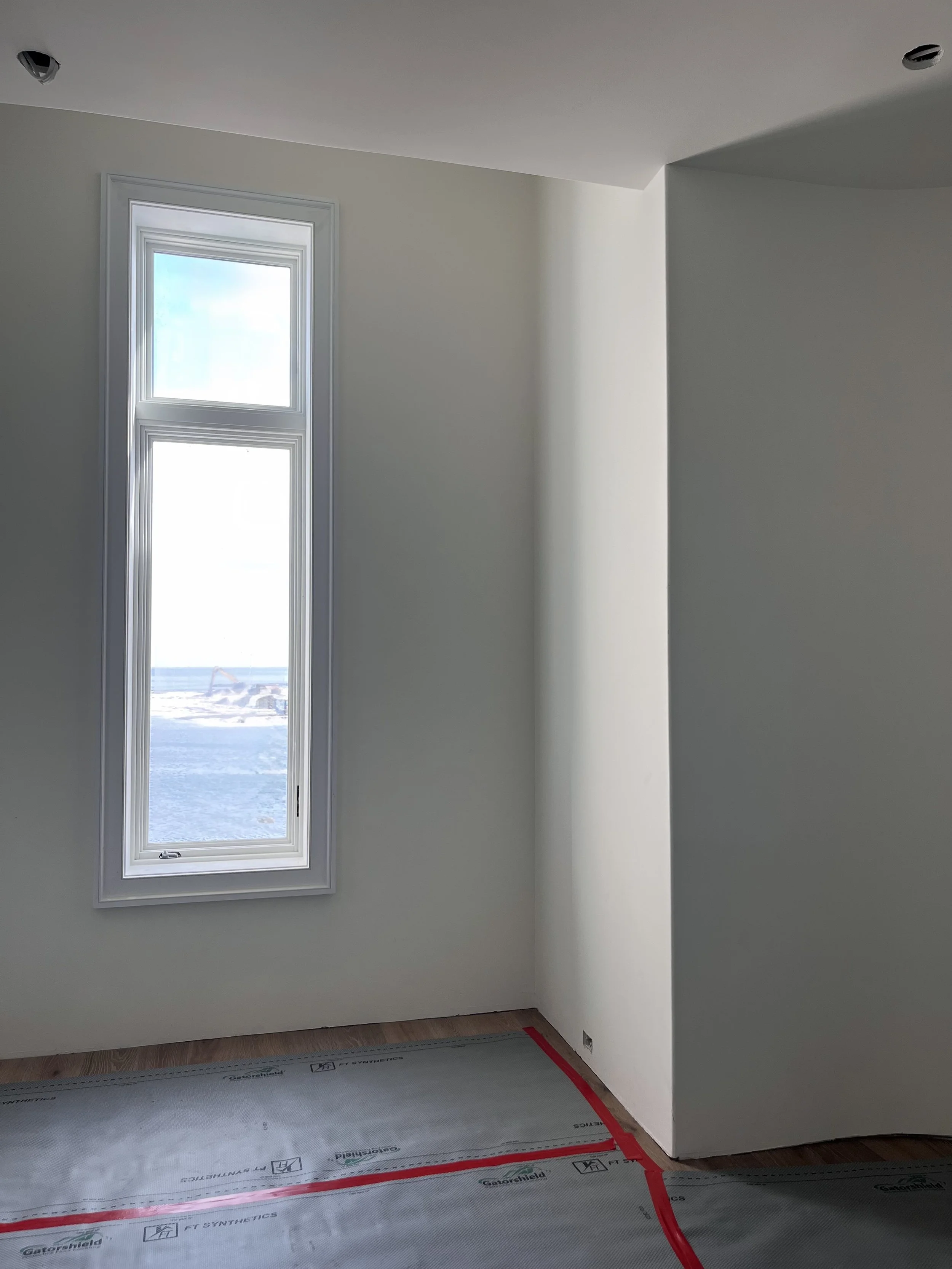 Empty room with a tall narrow window showing an outdoor scene and a partially curved wall, with the floor covered in protective material.