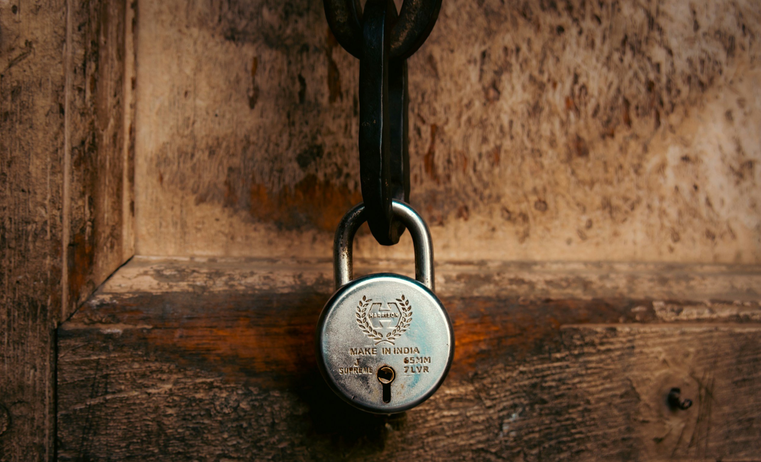 A silver padlock hanging from a black chain on a wooden surface.