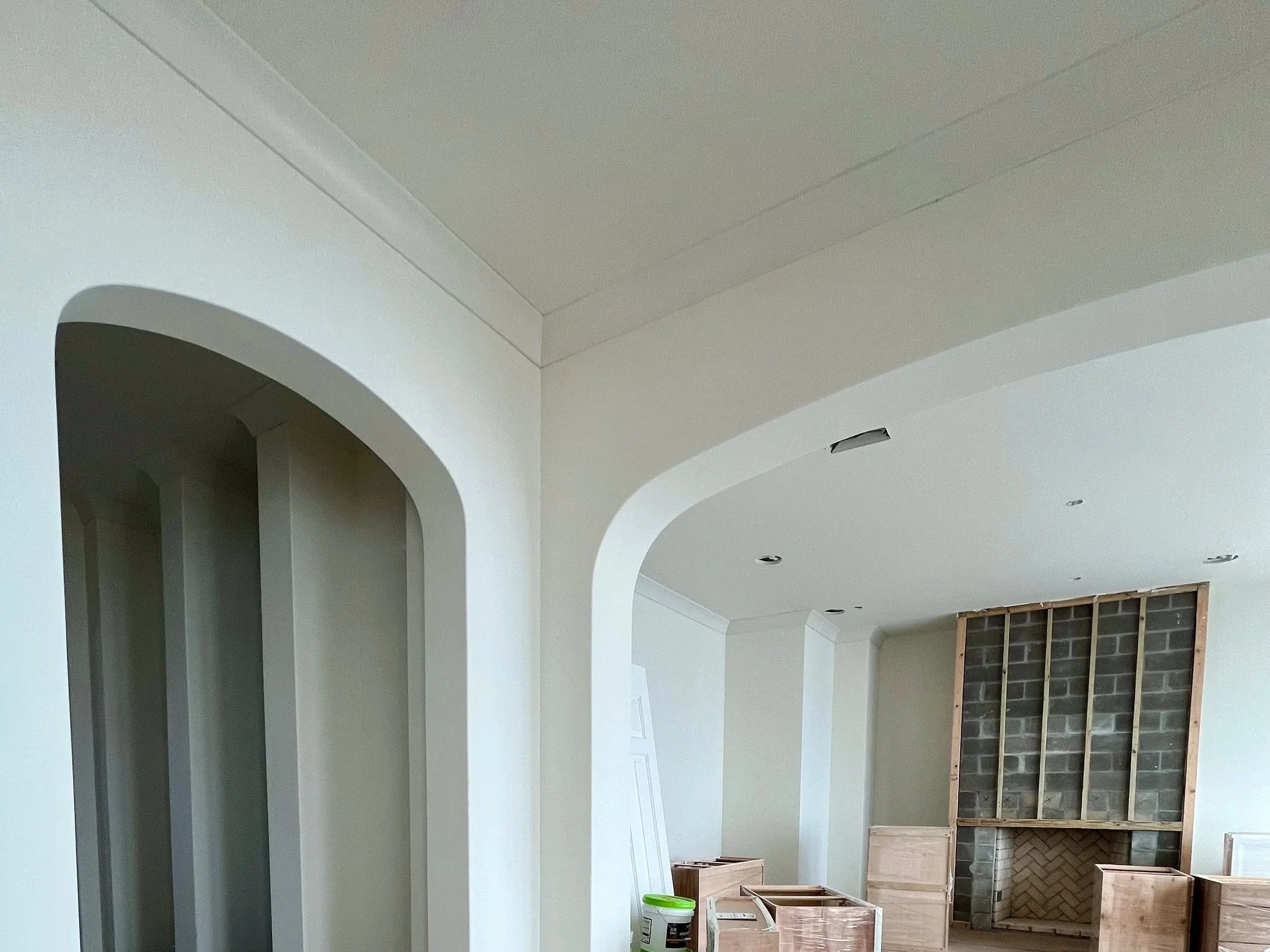 Interior of a house under construction with arched doorways, unfinished walls, and a fireplace framework made of cinder blocks and wood framing.