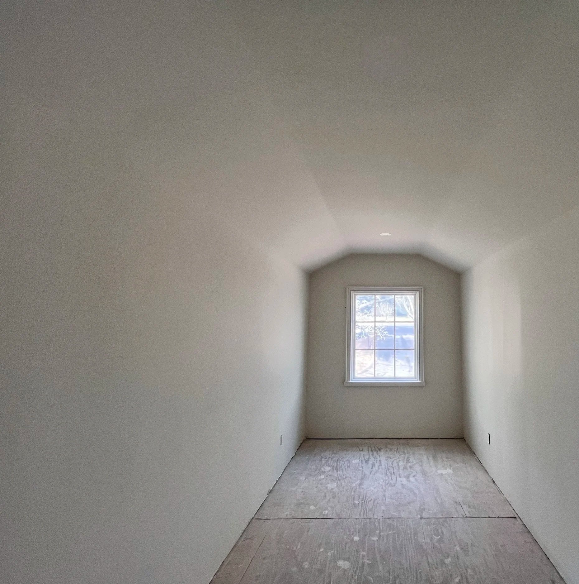 Empty attic room with a window at the far end, white walls, and bare floor.