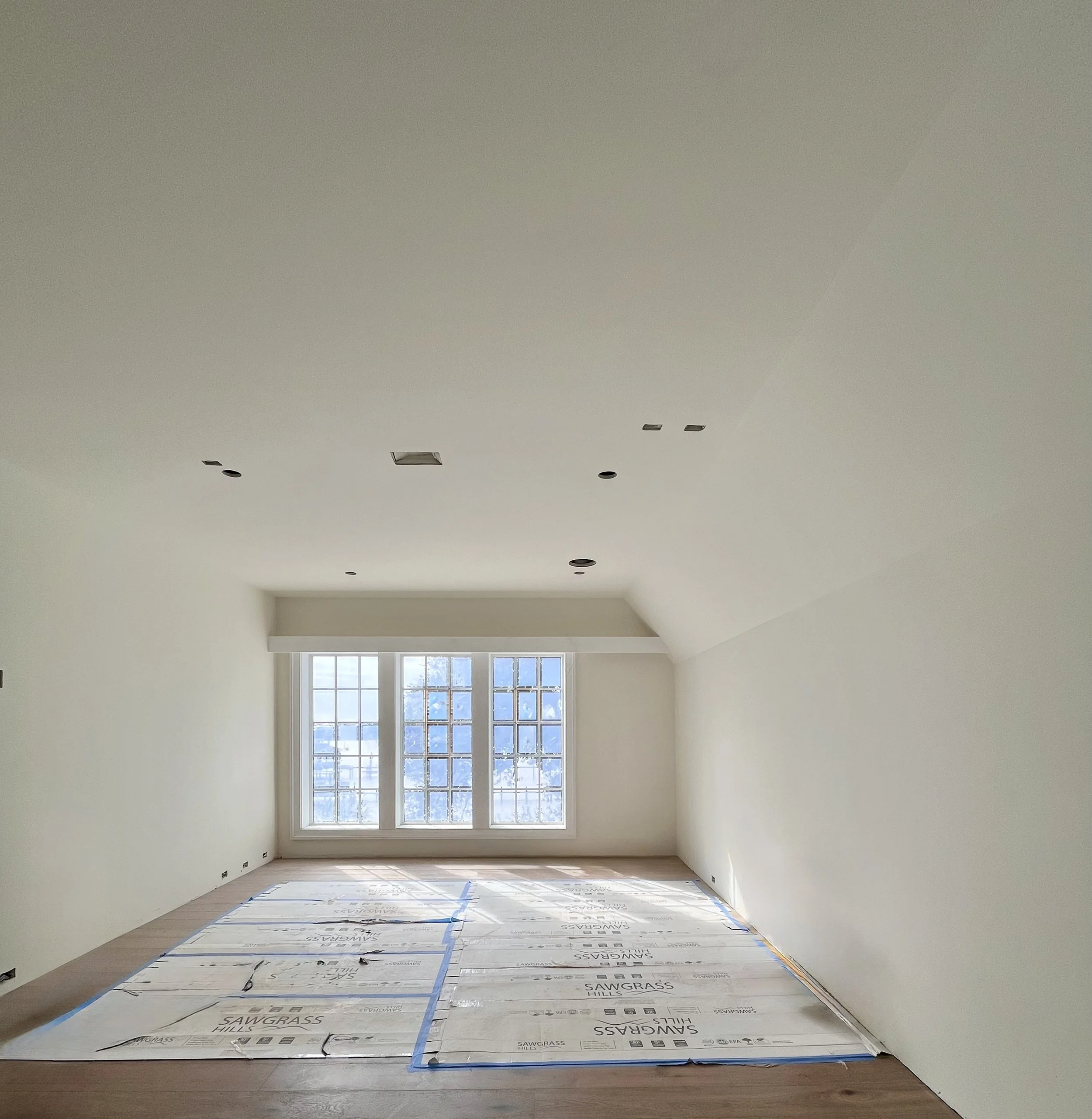 Empty room under construction with white walls and large window, covered floor with protective sheet.