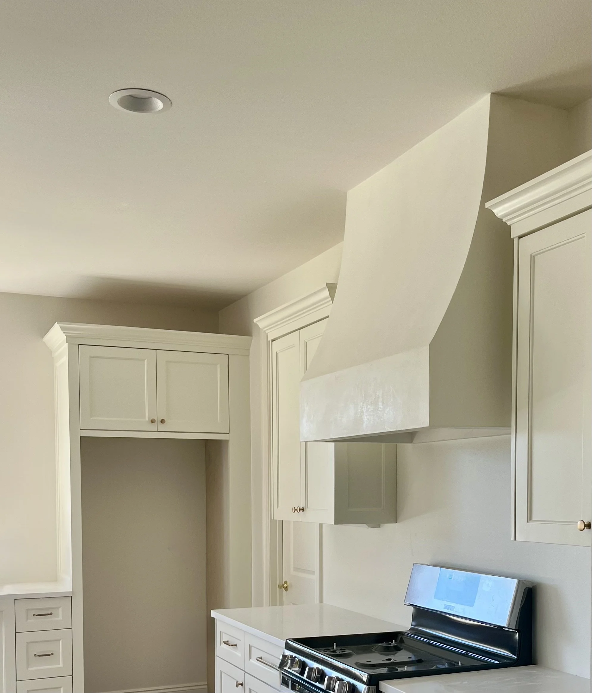 Kitchen with white cabinets and a stainless steel stove with a large white range hood above it.