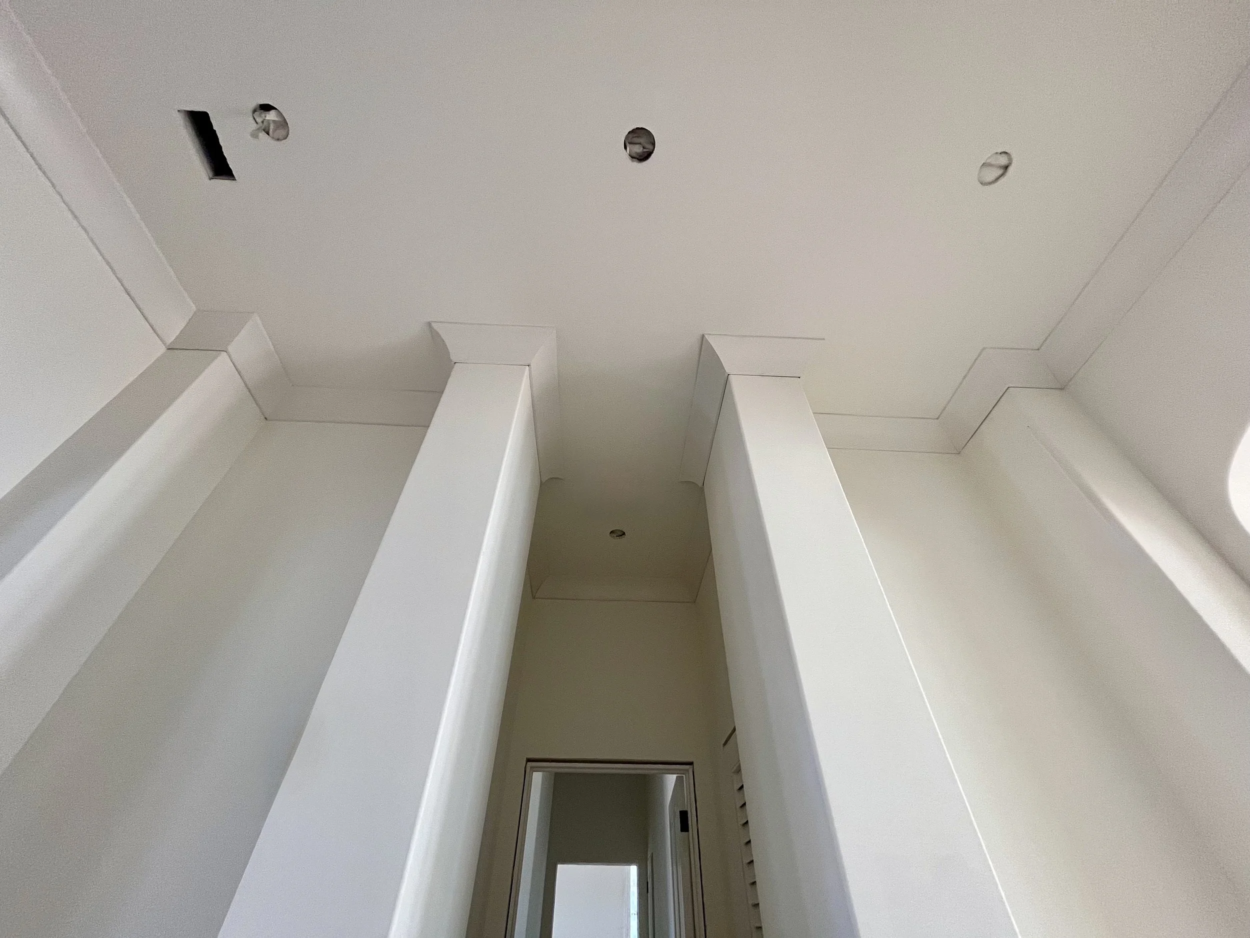 Partially finished ceiling with three circular light fixtures and a rectangular vent opening, painted white, with a doorway visible at the bottom of the image.