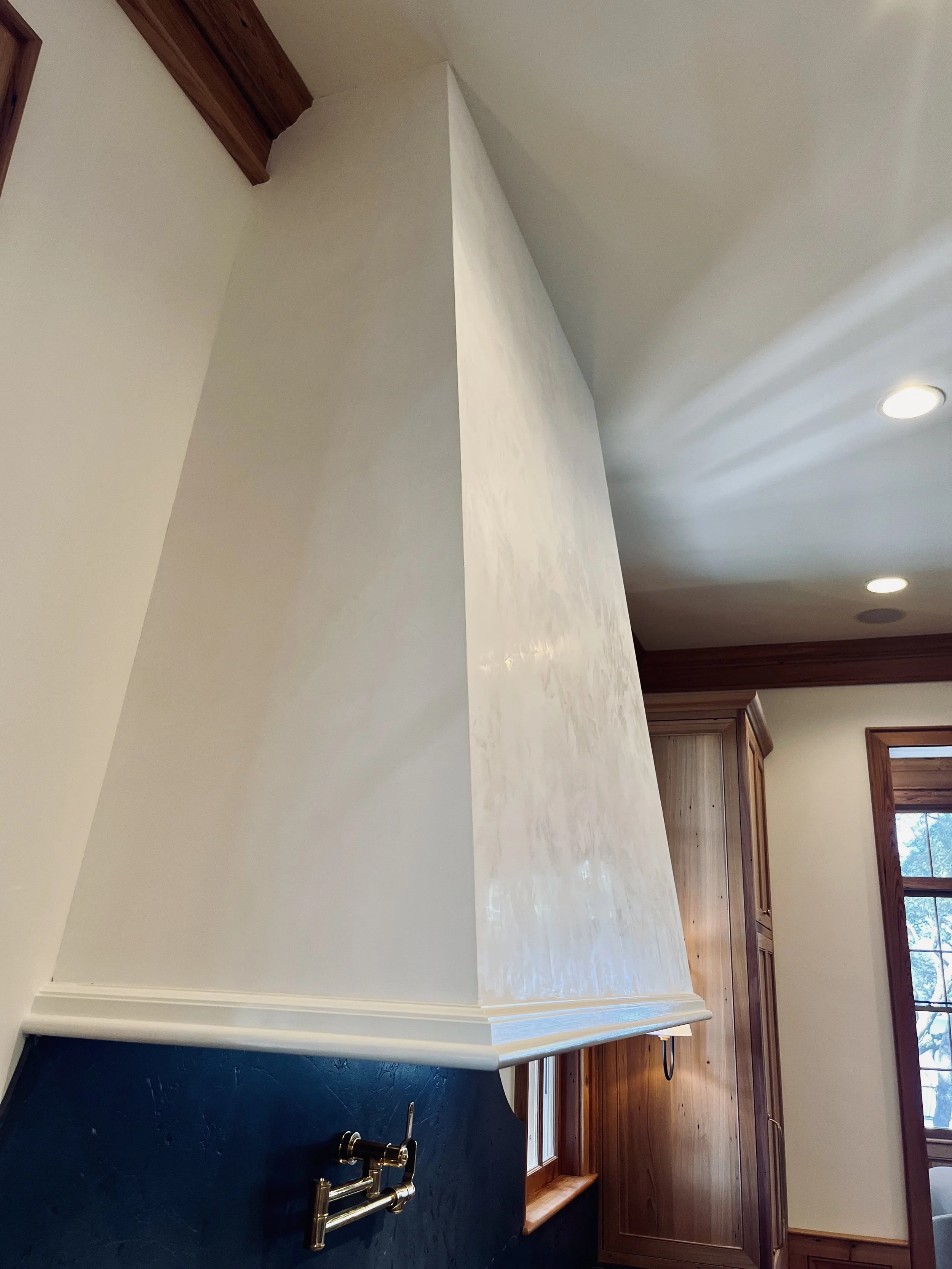 A kitchen with a beige range hood, wooden cabinets, a window, and a faucet.
