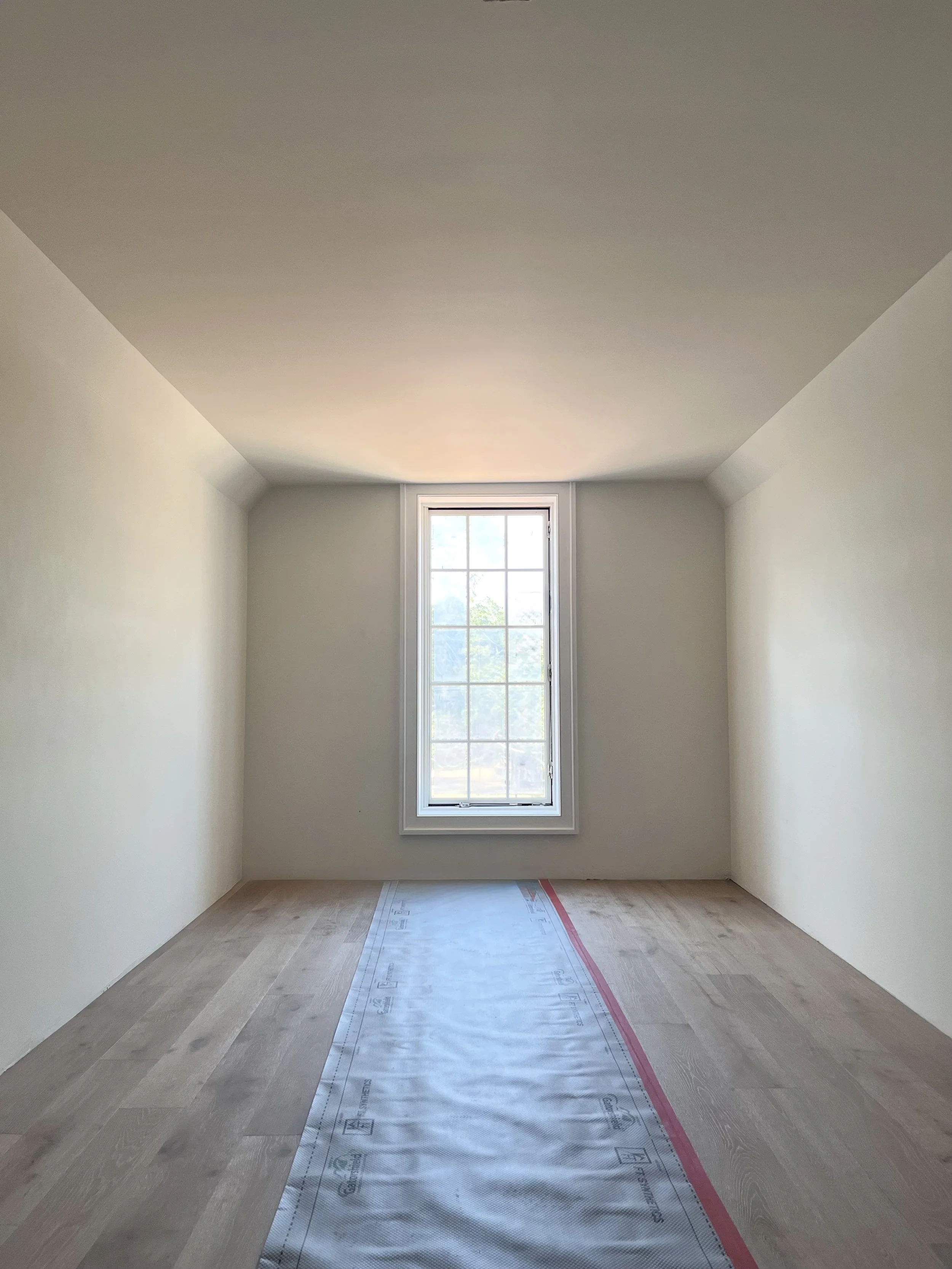 Empty room under renovation with a window and a protective sheet on the wooden floor.