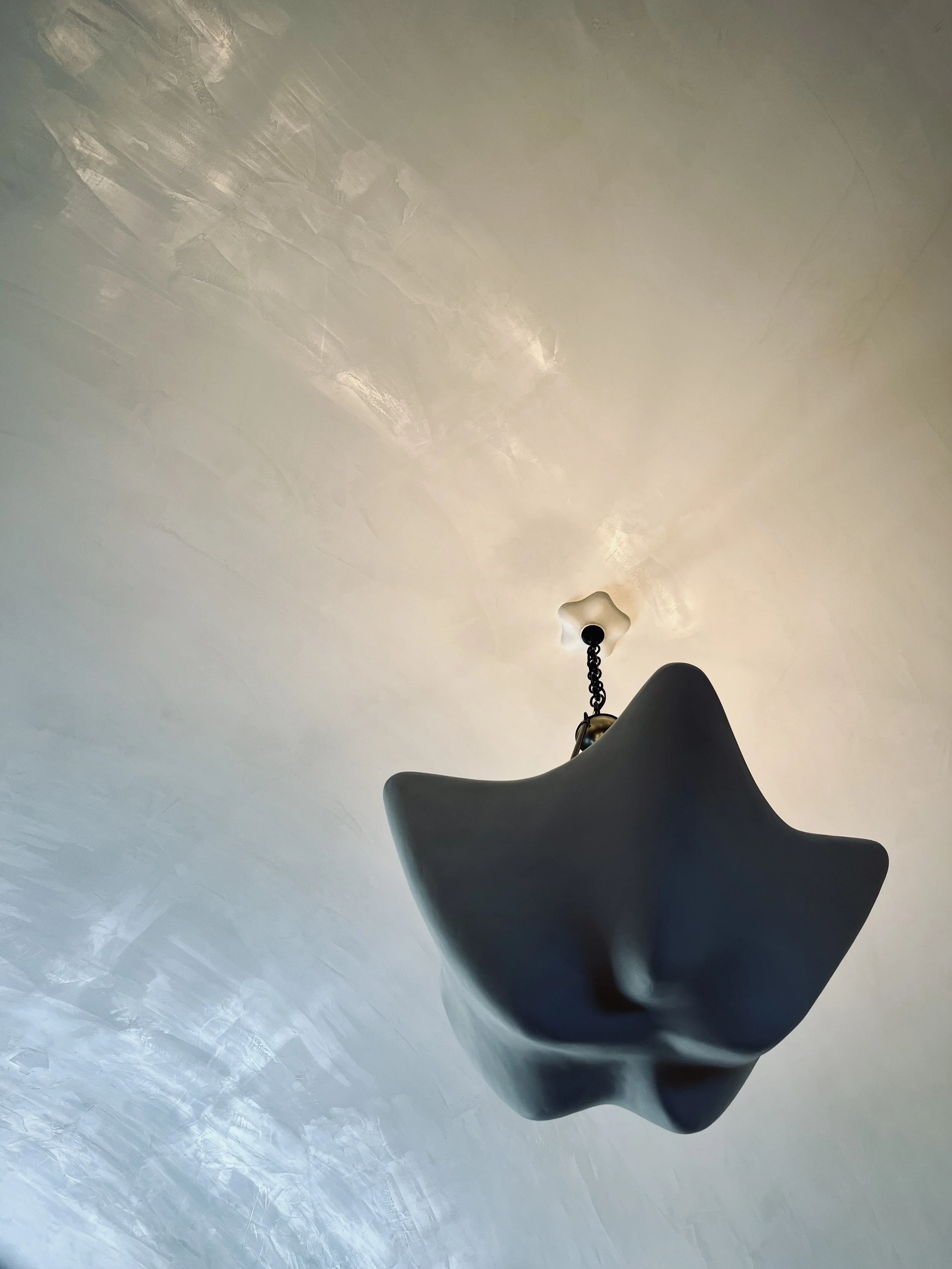 A black star-shaped chandelier hanging from a chain attached to a white ceiling.