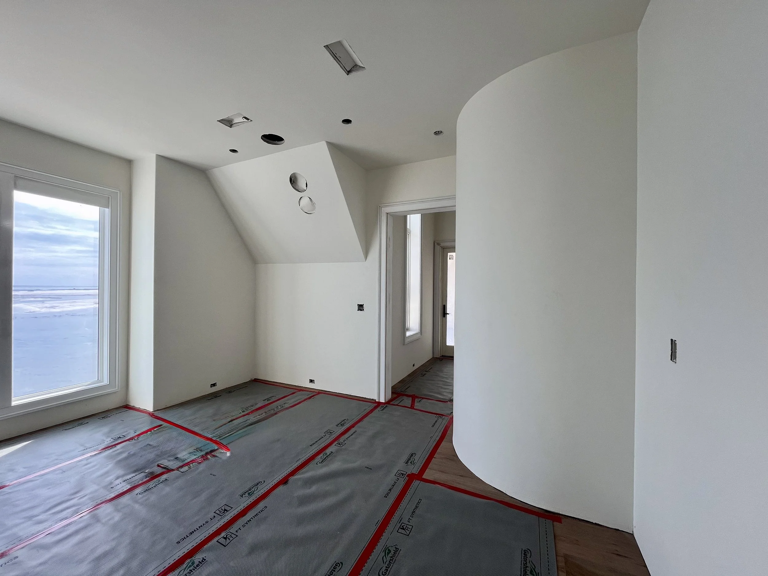 Interior of a house under construction with white walls, large window viewing a snowy landscape, and protective floor covering.