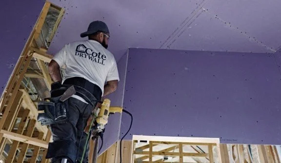 Construction worker installing purple drywall in a room under construction.