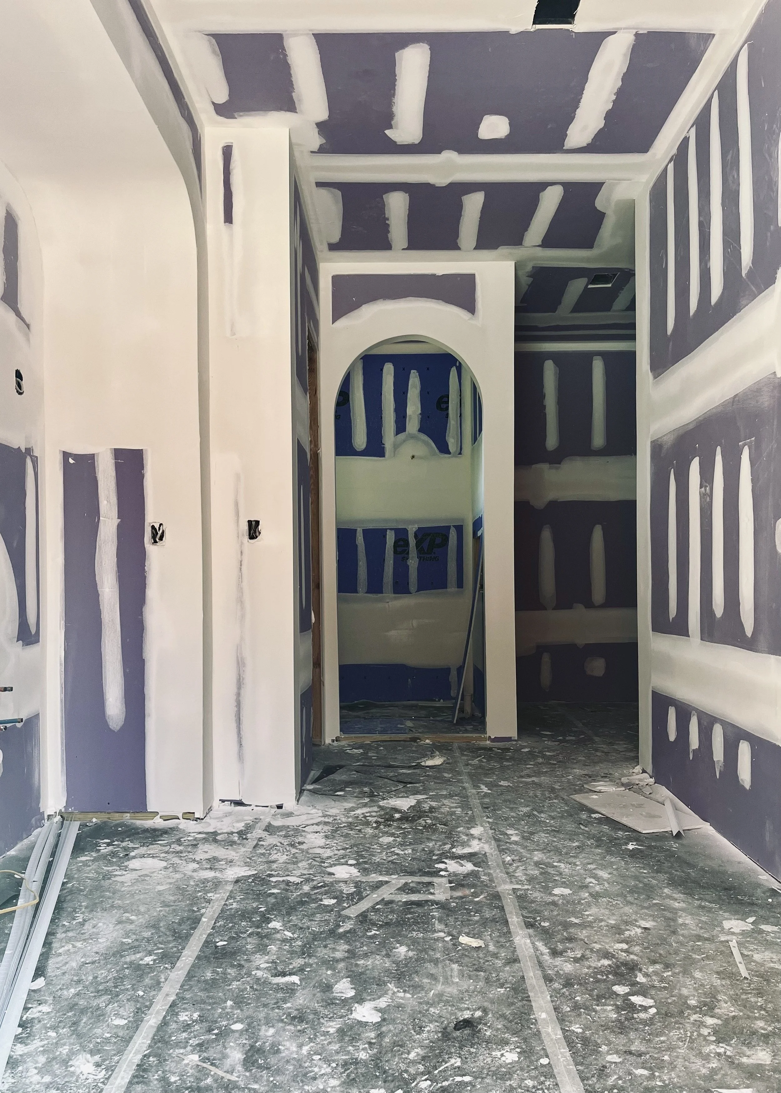 Interior of a room under construction with drywall installation and finishing in progress, including taped and mudded seams on walls and ceiling.