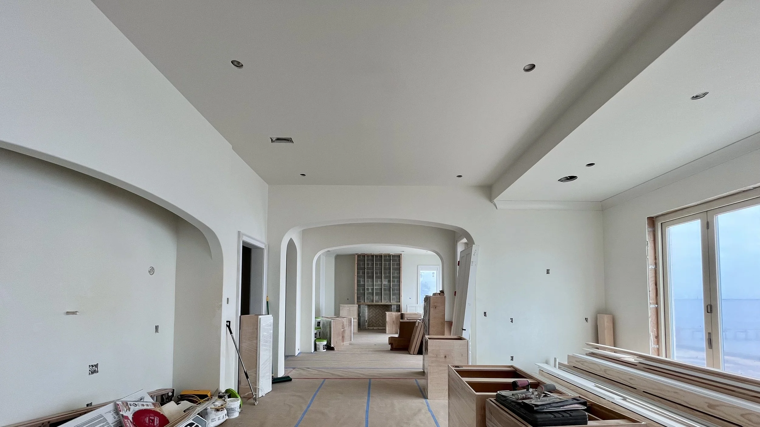 Interior of a house under construction or renovation, with unfinished walls, ceiling, and built-in furniture, and construction tools and materials scattered around.