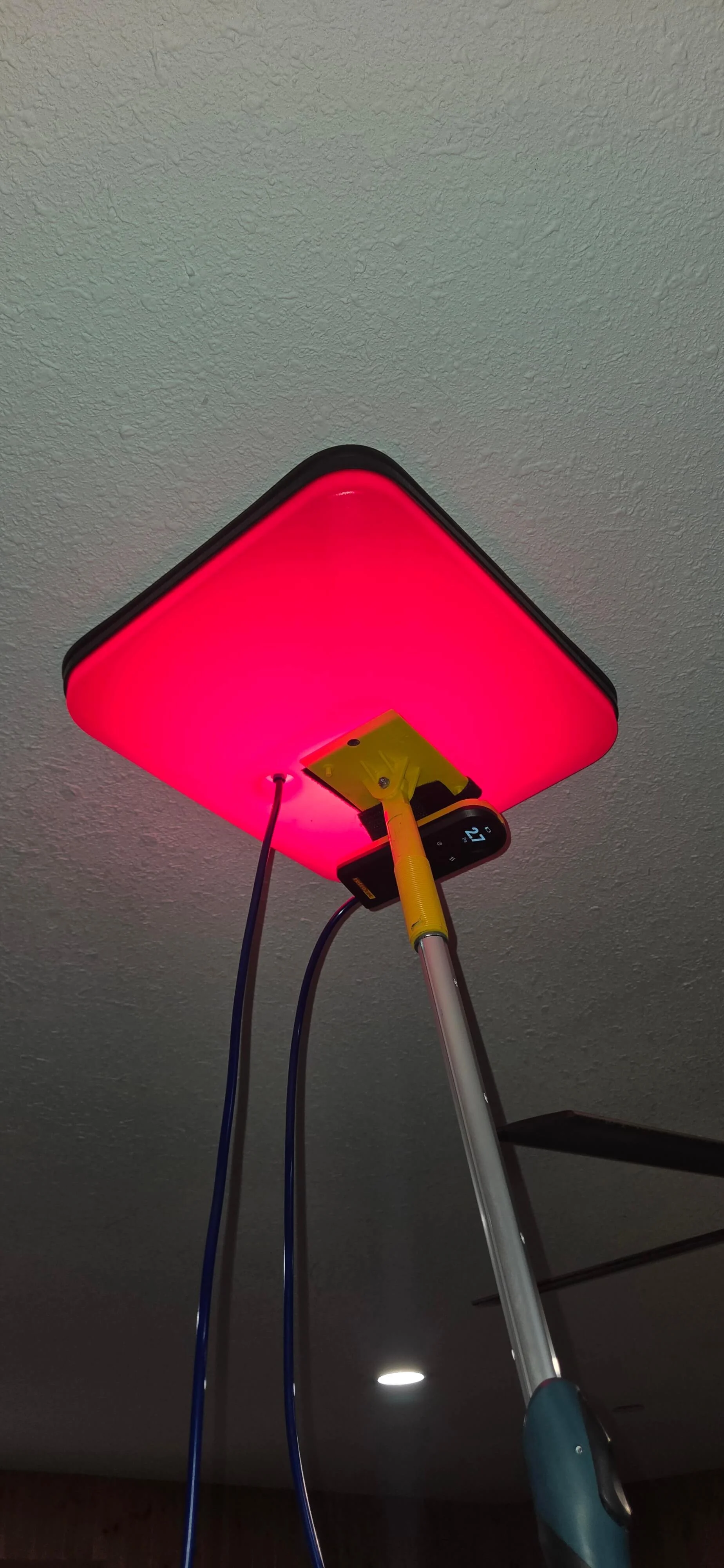 A medical or therapeutic device emitting red light, mounted on a metallic stand with a digital display showing '21', connected to two blue cables.