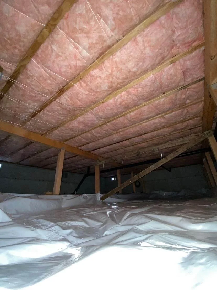 Pink fiberglass insulation and heavy-duty white vapor barrier in residential crawl space.