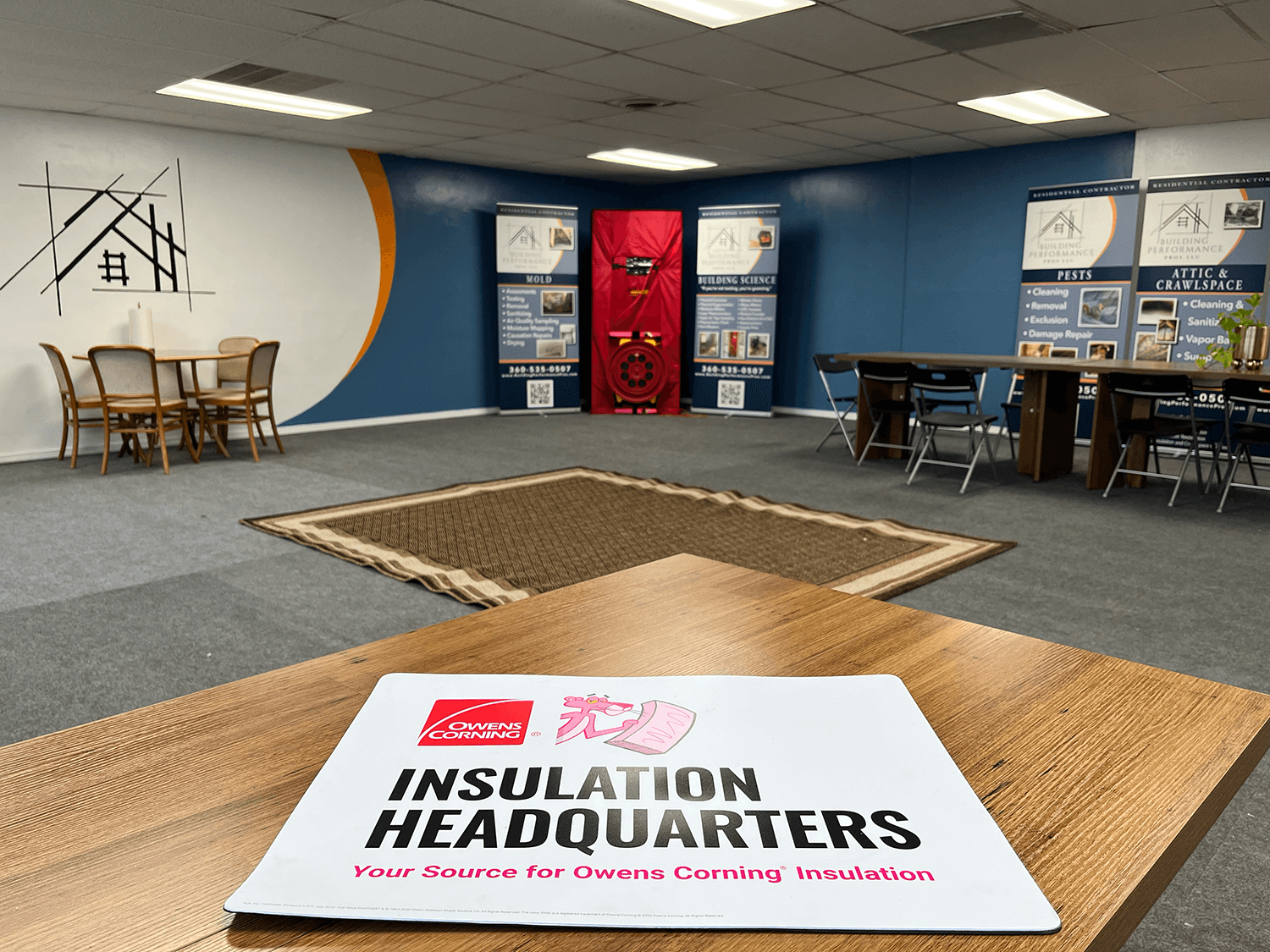 Interior of Building Performance Pros Headquarters with Owens Corning binder on a table in the foreground. Customer area with chairs, signage, and informational boards in the background.