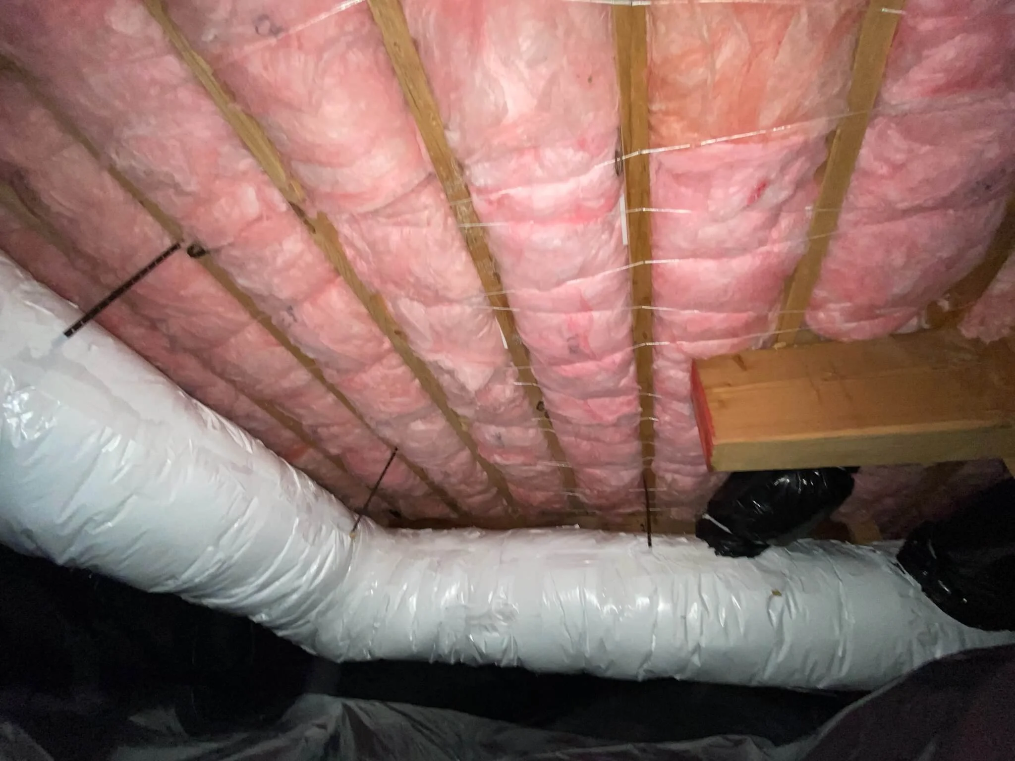 Pink fiberglass insulation professionally installed in residential crawl space with wrapped ductwork.