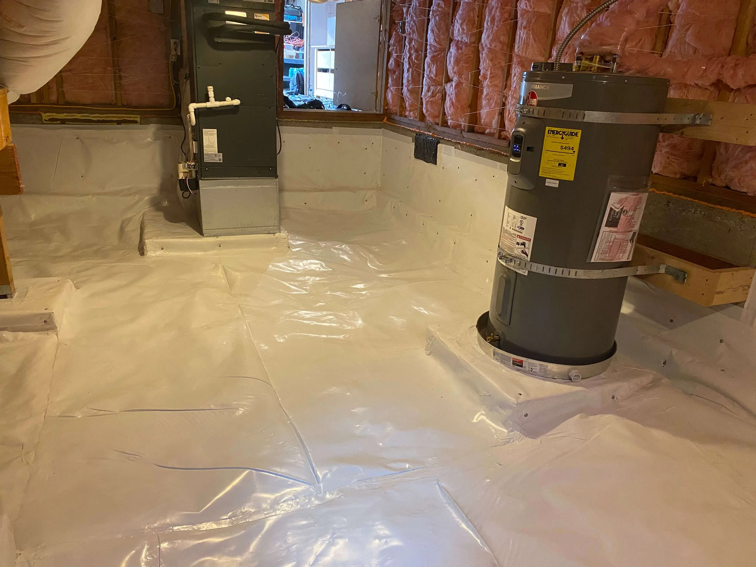 Residential basement with proper encapsulation. Showing ductwork, heating system, and insulation installed, with white plastic vapor barrier on the floor.