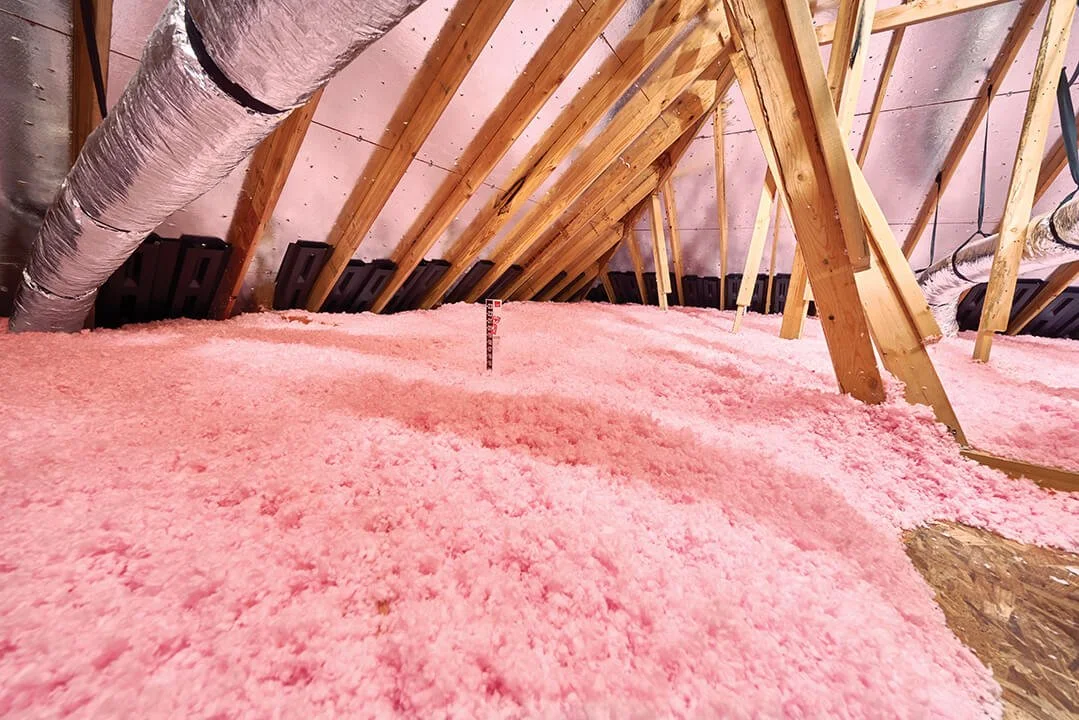 Pink blown-in insulation on attic floor with exposed wooden beams and wrapped ductwork.