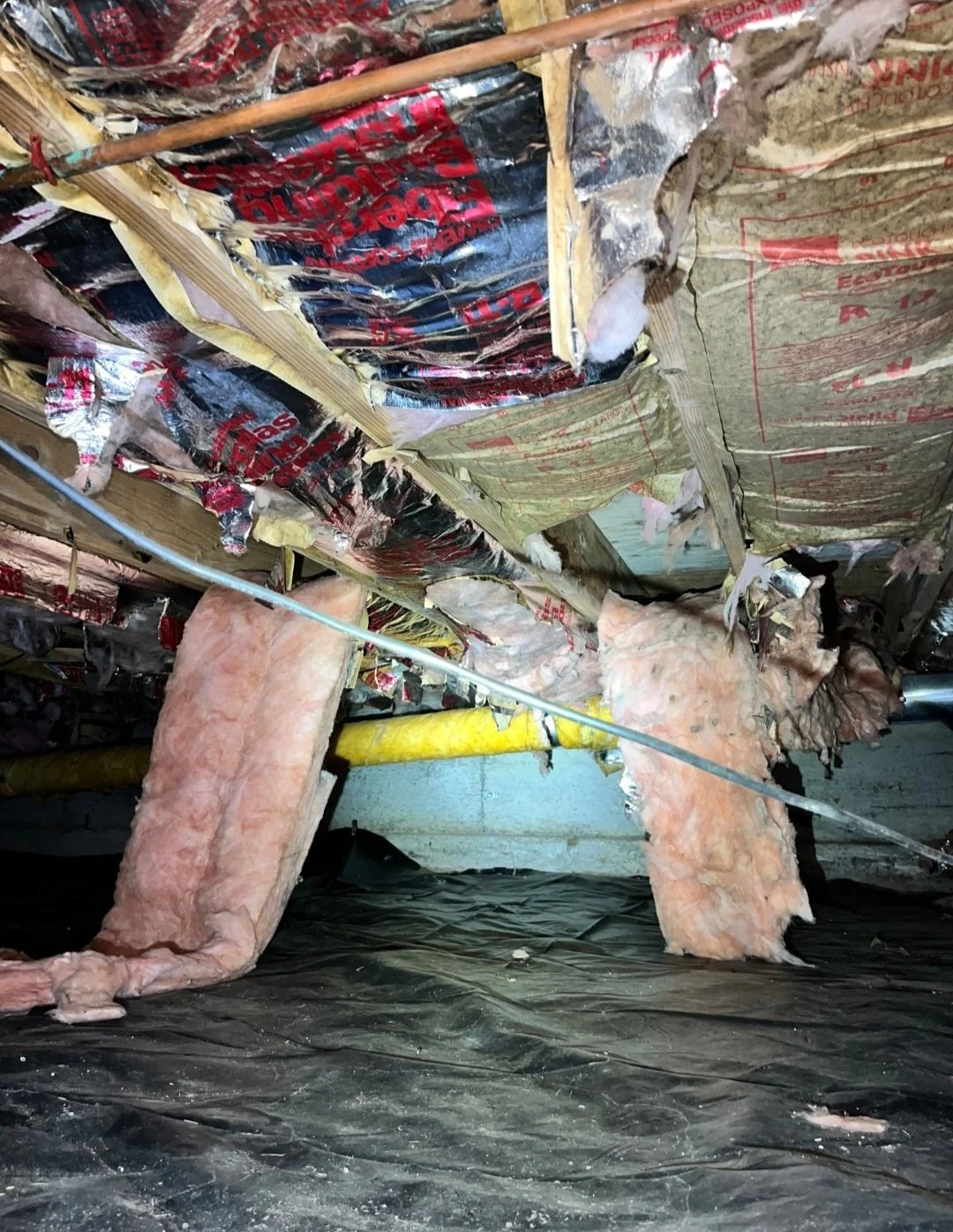 Insulation installed in a ceiling with pink fiberglass bats held in place by wooden beams and a metal rod passing through.