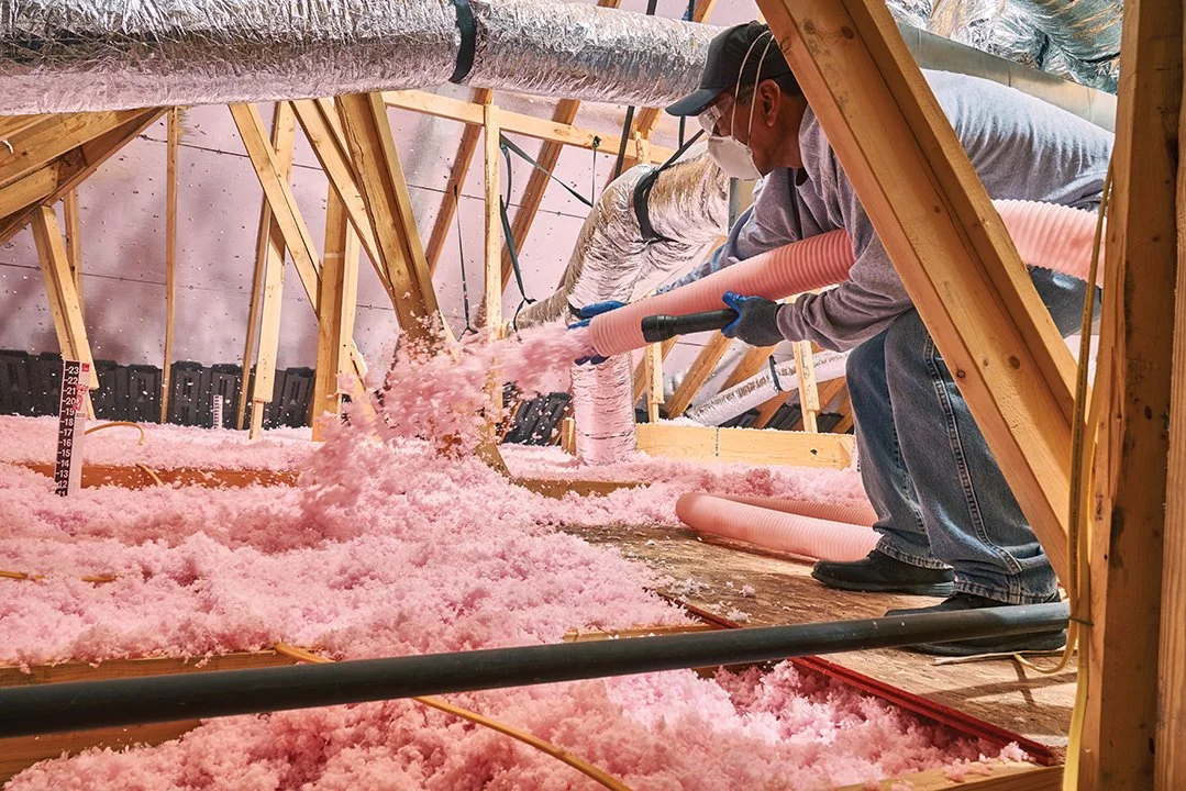 Professionally trained technician installing blown-in pink insulation in a residential home attic.