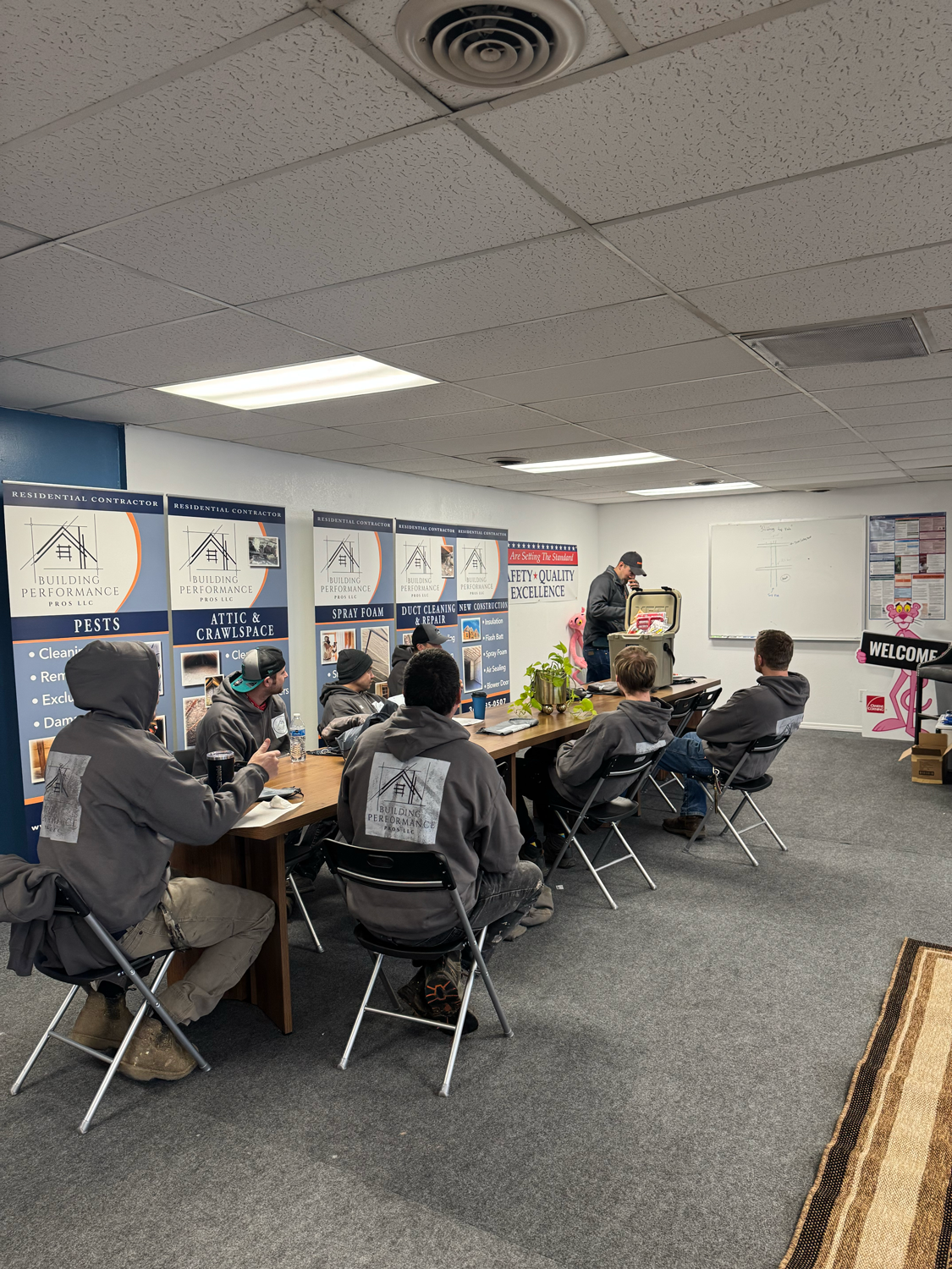 Building Performance Pros technician training session. Group is in matching hoodies attending meeting in conference room with promotional banners on the walls.