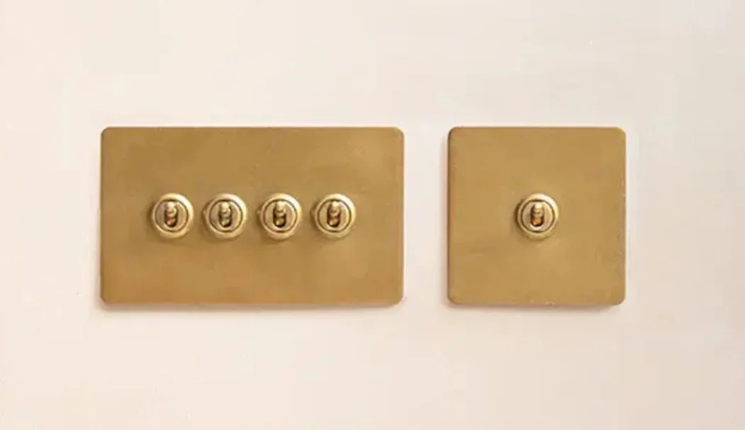 A gold-colored four-switch panel and a single-switch panel on a cream wall.