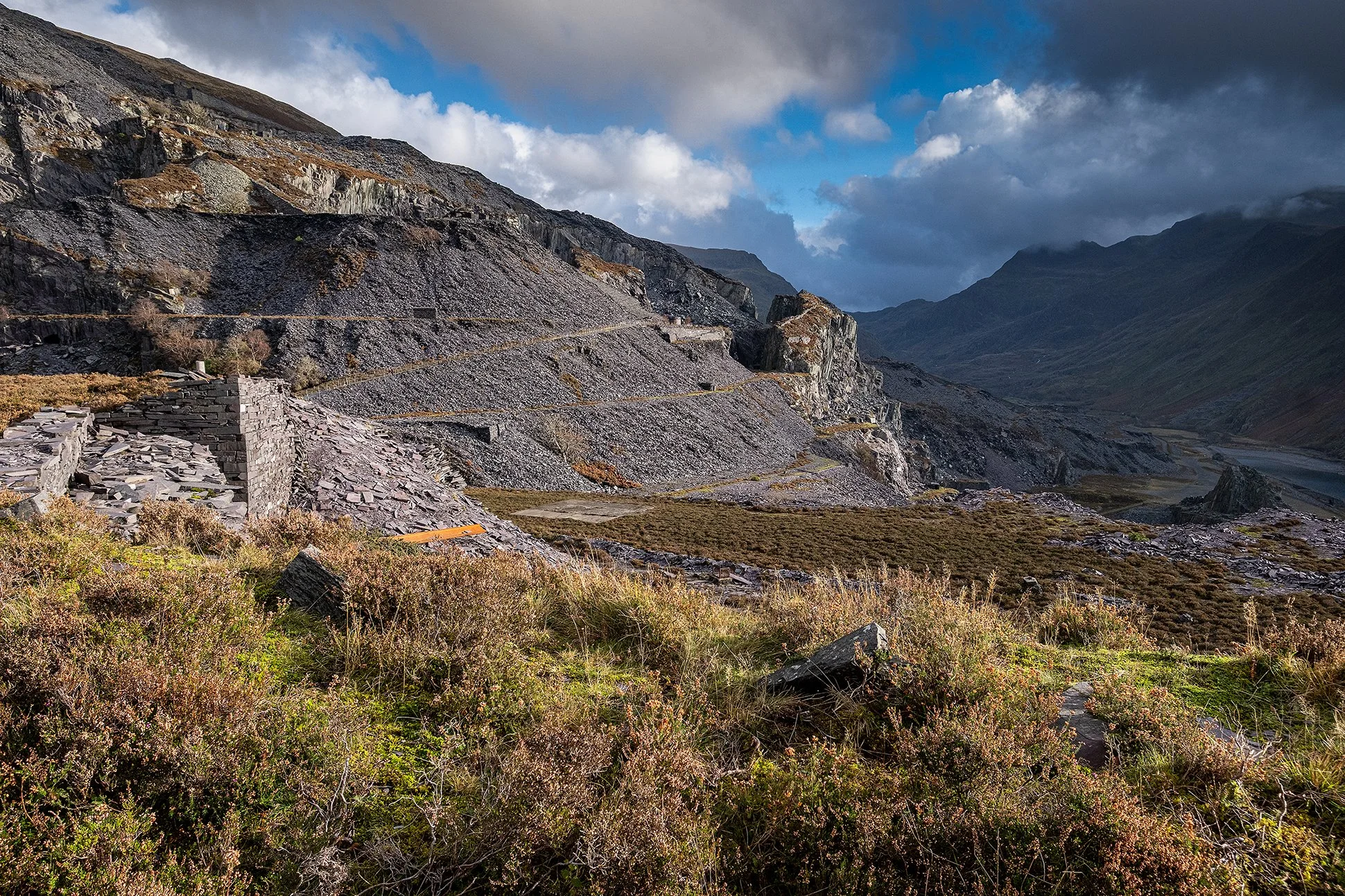 Rugged mountain landscape with terraced slopes, stone structures, and cloudy sky.
