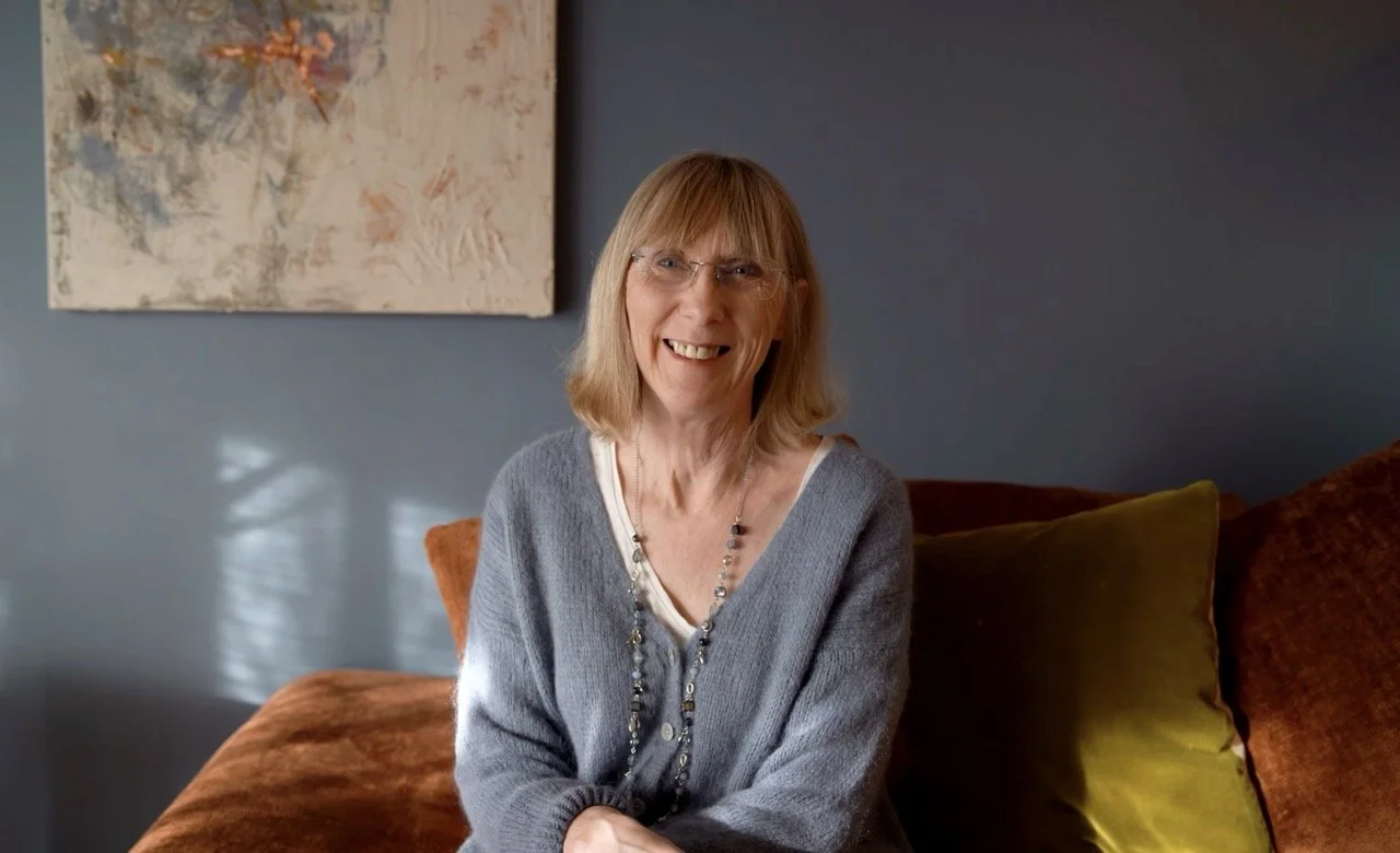 female wearing soft grey blue with a background of grey blue and a picture in the background