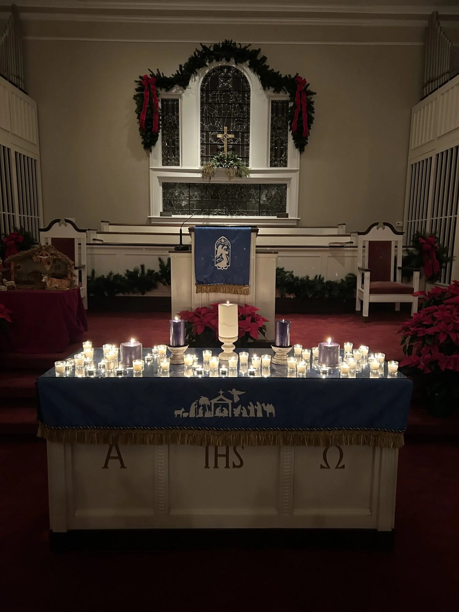 Christmas decorated church altar with candles, poinsettias, and religious symbols.