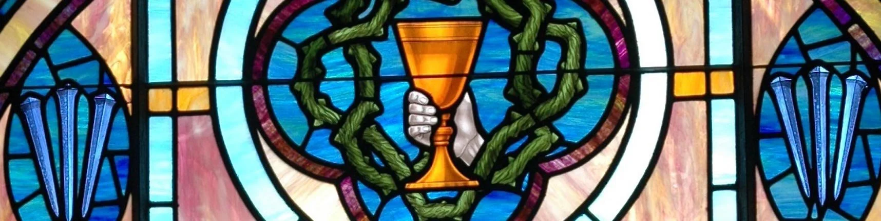 Stained glass window depicting a hand holding a chalice surrounded by vines and blue decorative elements.
