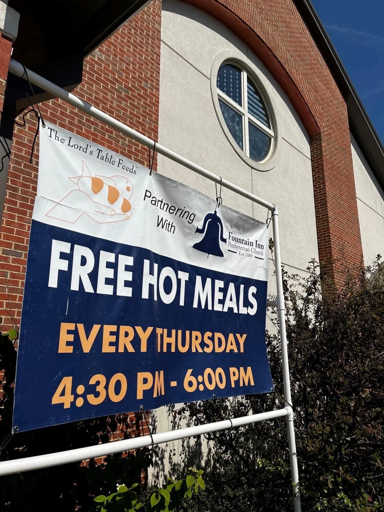Sign advertising free hot meals every Thursday from 4:30 PM to 6:00 PM, partnering with Fountain Inn Presbyterian Church, with a logo of a fish and a bell.