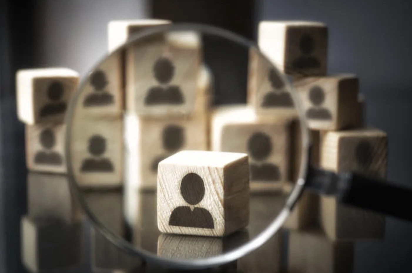 There are wooden blocks with user icons on them, viewed through a magnifying glass.