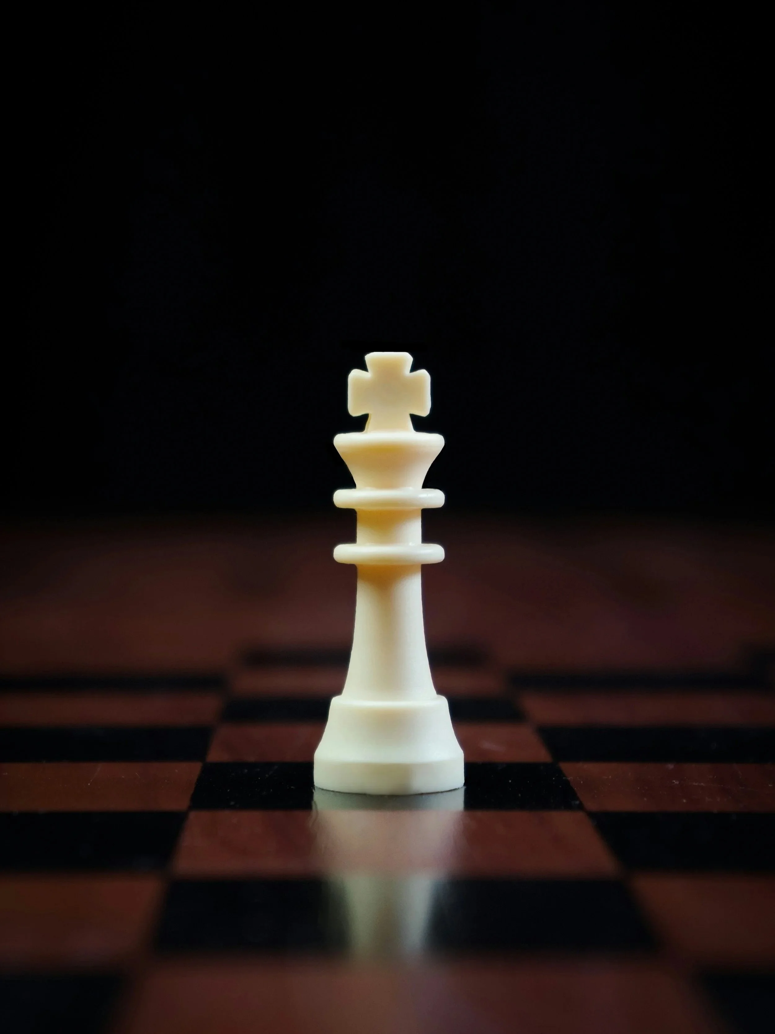 White king chess piece on a checkered chessboard with a black background.