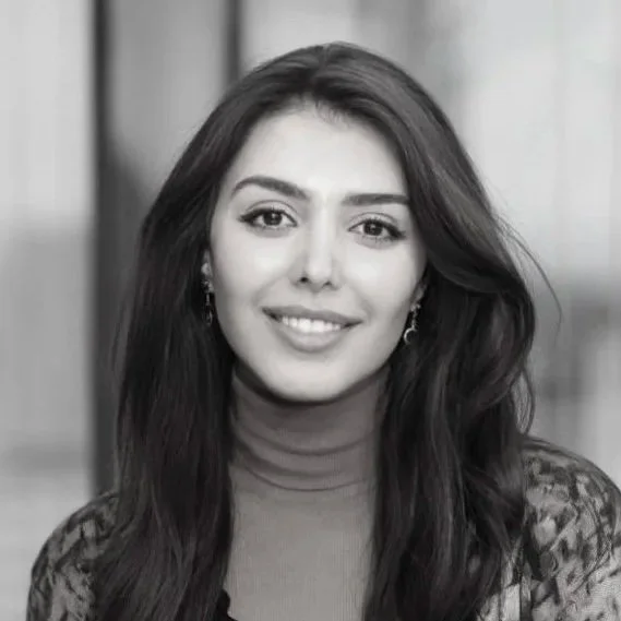 Black and white portrait of a smiling woman with long wavy hair, wearing earrings and a turtleneck sweater.